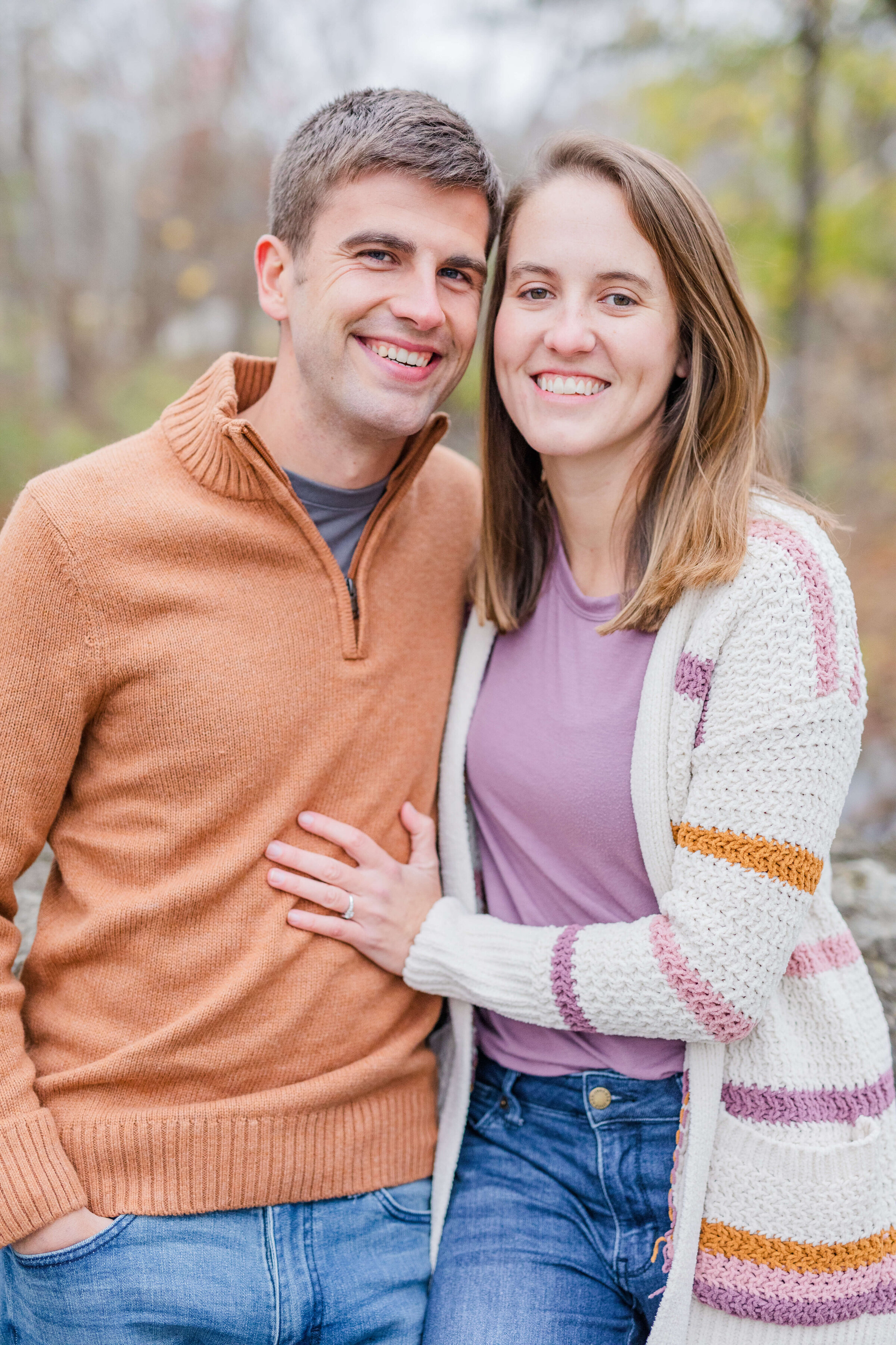 A man and woman stand next to each other smiling at the camera. They are in orange and purple sweaters