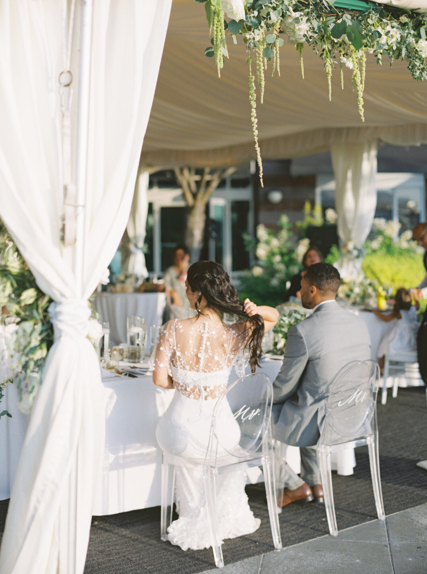 bride and groom sit in ghost chairs with custom calligraphy in white on the back