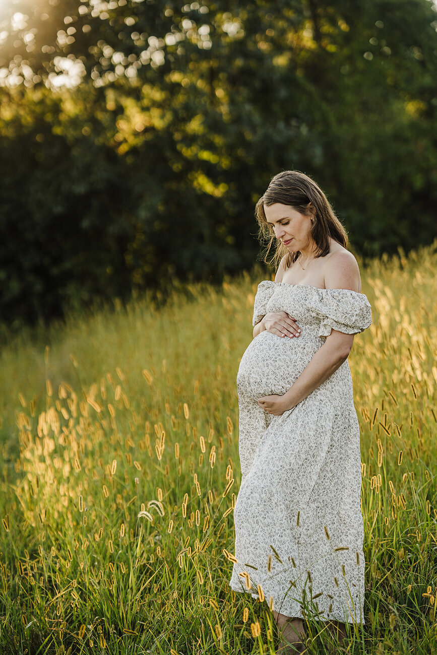 woman in cream maternity dress poses in boston field