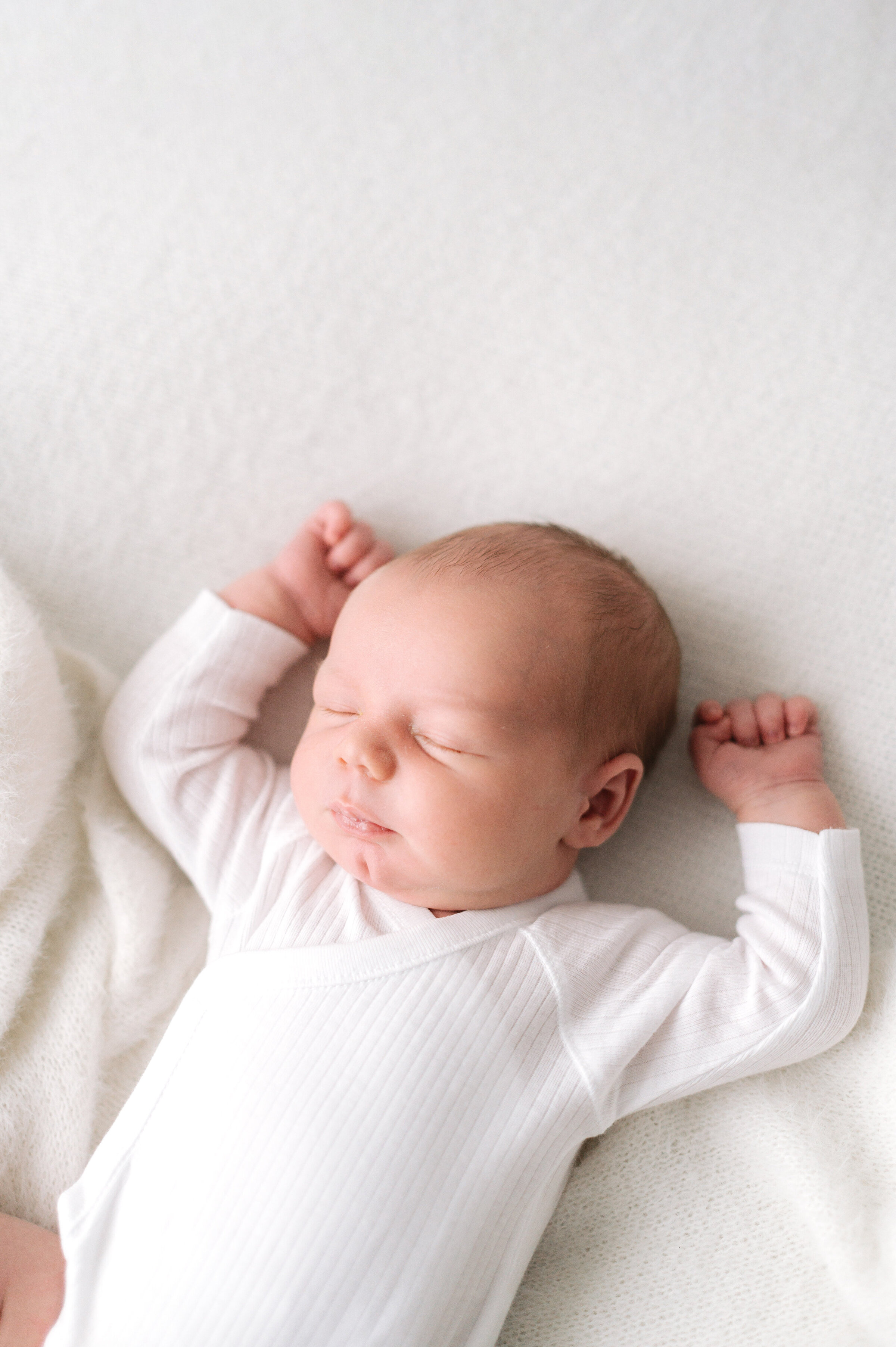 Newborn baby boy sleeping with his arms up by his head at newborn photoshoot in Billingshurst