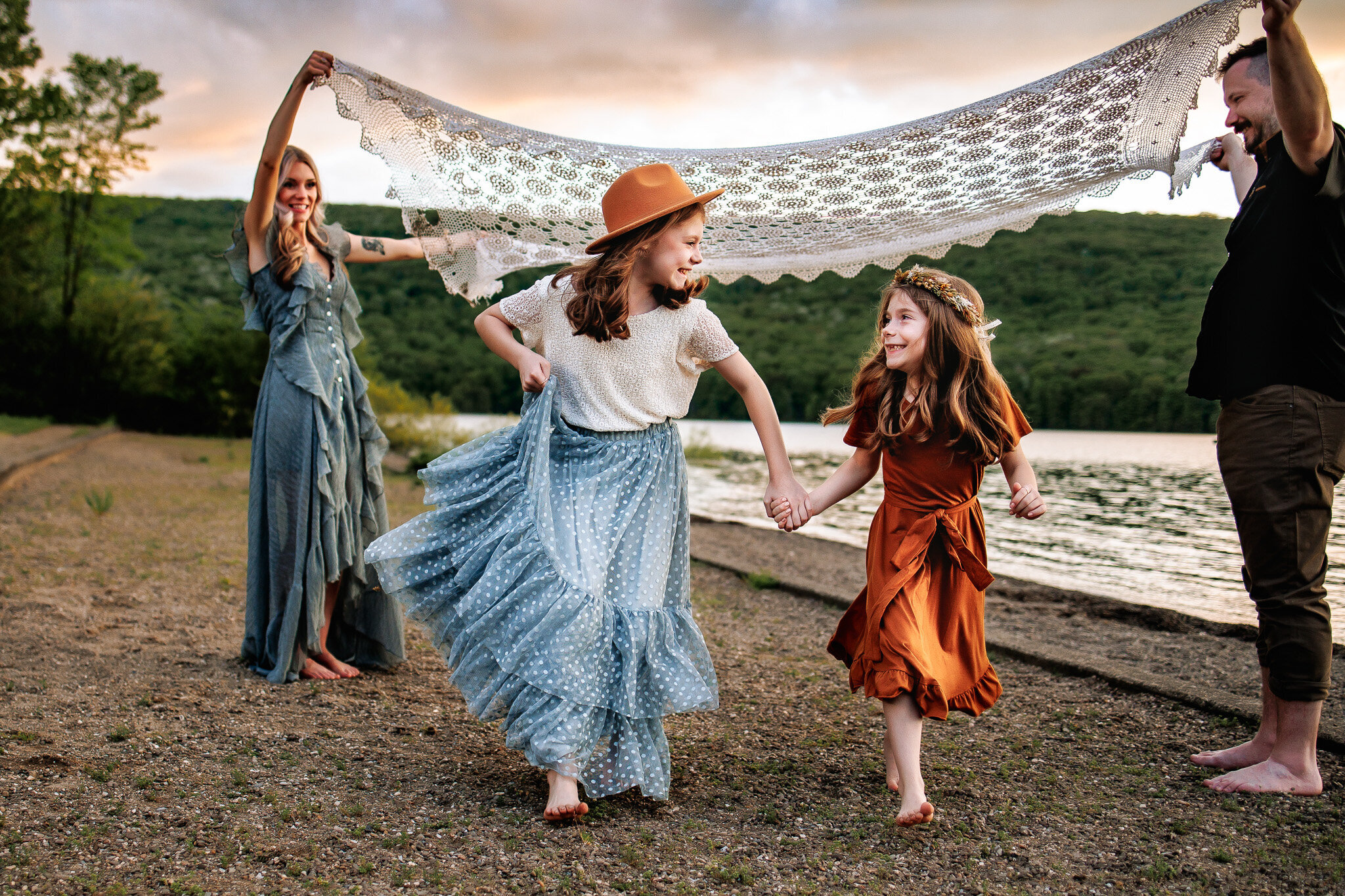 Joyful family portrait at sunset: family dancing on lakeside shore with scenic hills and lake backdrop