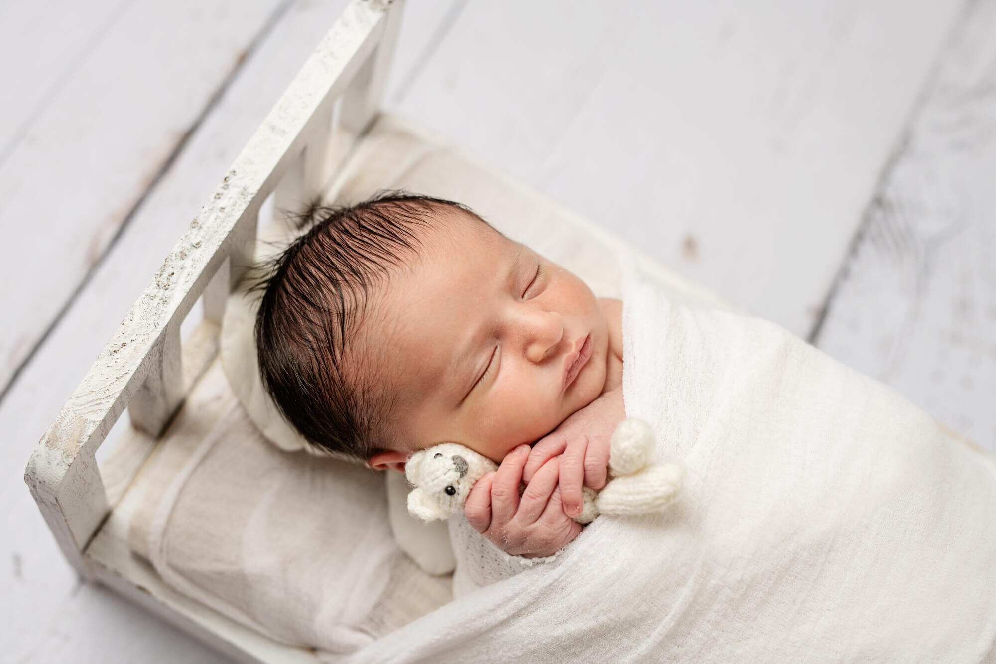 Sleeping baby in white bed with white teddy bear