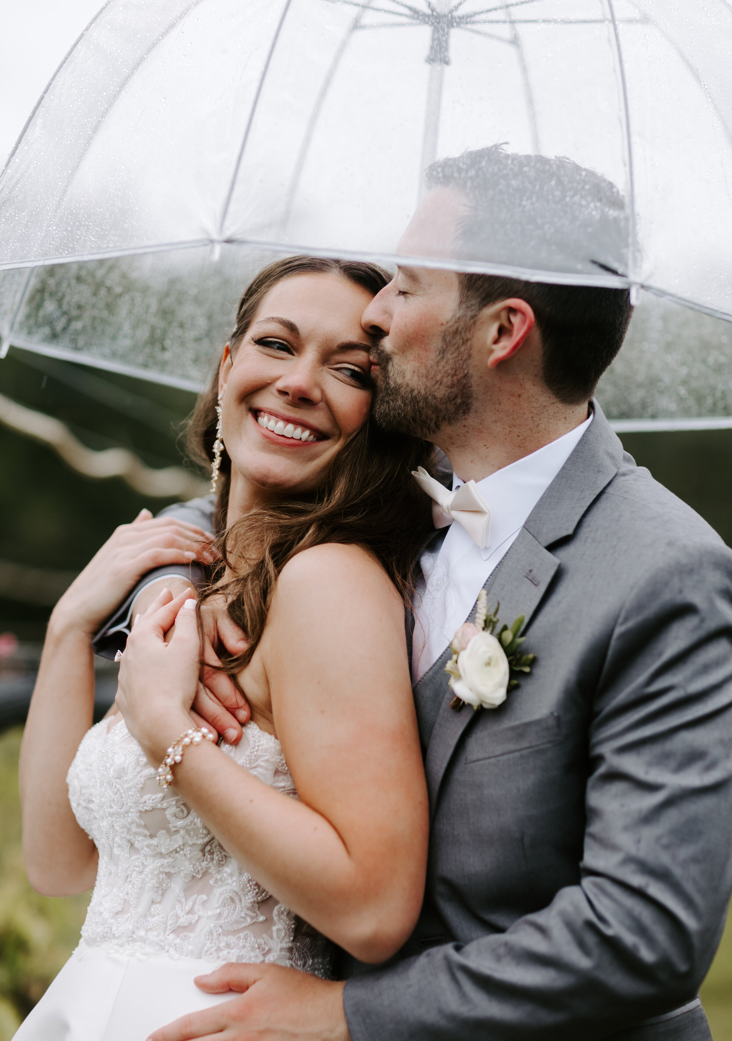 Bride leans into groom under umbrella during rainy wedding at Labelle Winery in Amherst, New Hampshire