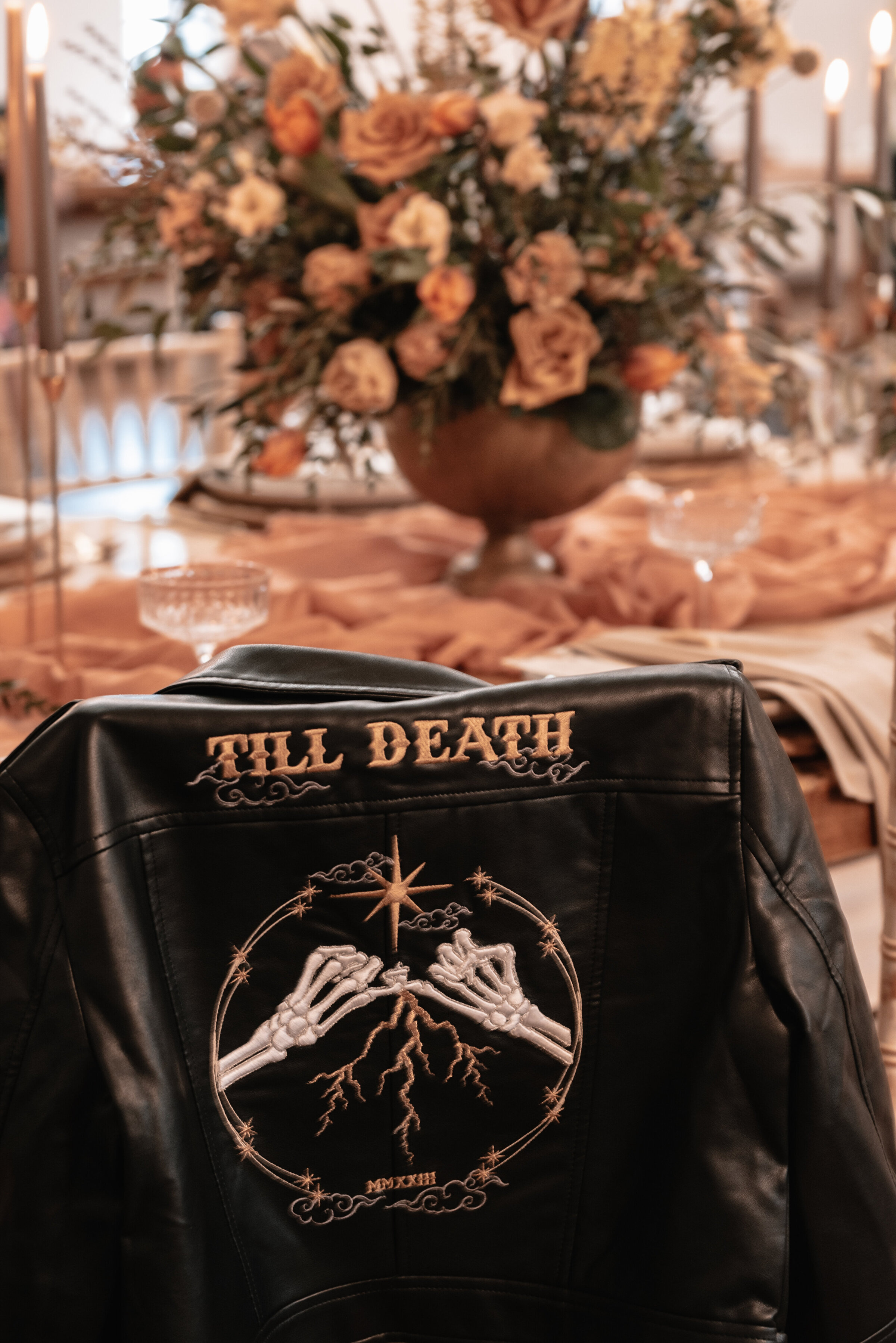 Leather bridal jacket embroidered with till death and skeleton hands holding pinkie fingers in front of floral arrangement