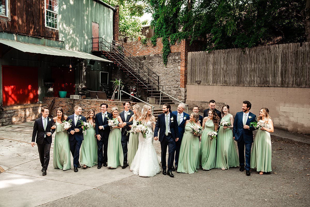 Wedding party walking in a line together in the back lot of Cannery , girls wearing a mint green full length dress and groomsmen are wearing a deep navy