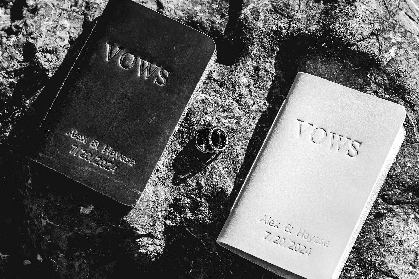 a black and white detail shot of vow books and wedding rings scattered on a textured rock to show the fine details of this adventure elopement.