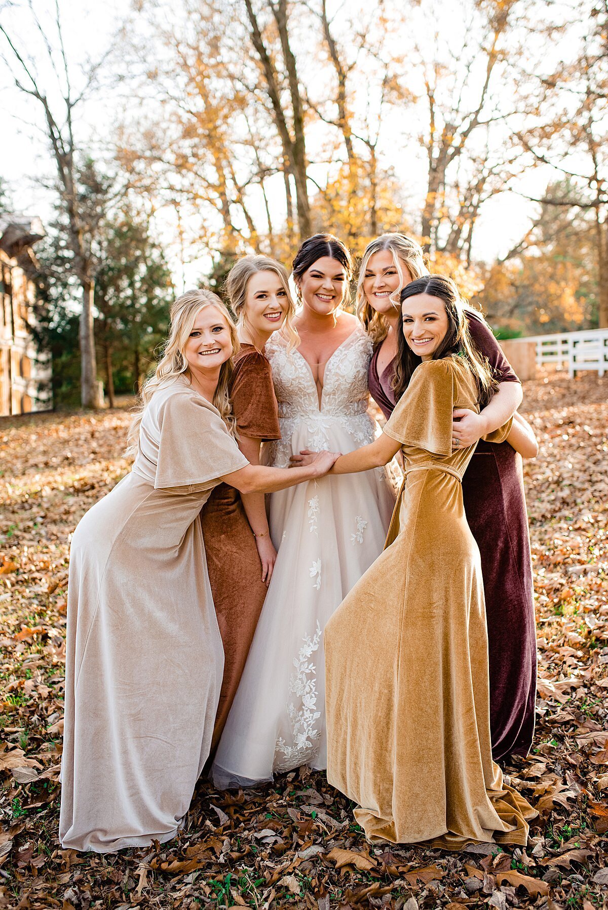 Bridesmaids wearing velvet dresses in autumn shades standing on leaves