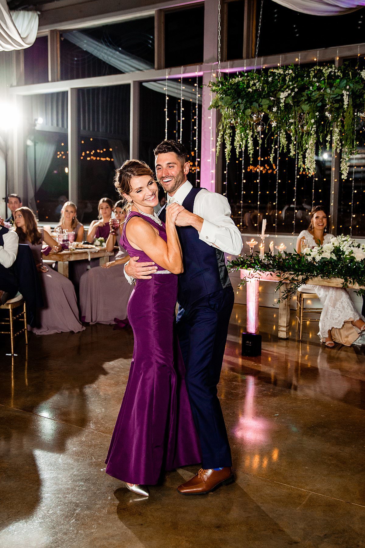 Mother of the Groom wearing an elegant purple taffeta form fitting dress with mermaid flair dancing with her son on the dance floor at Drakewood Farm