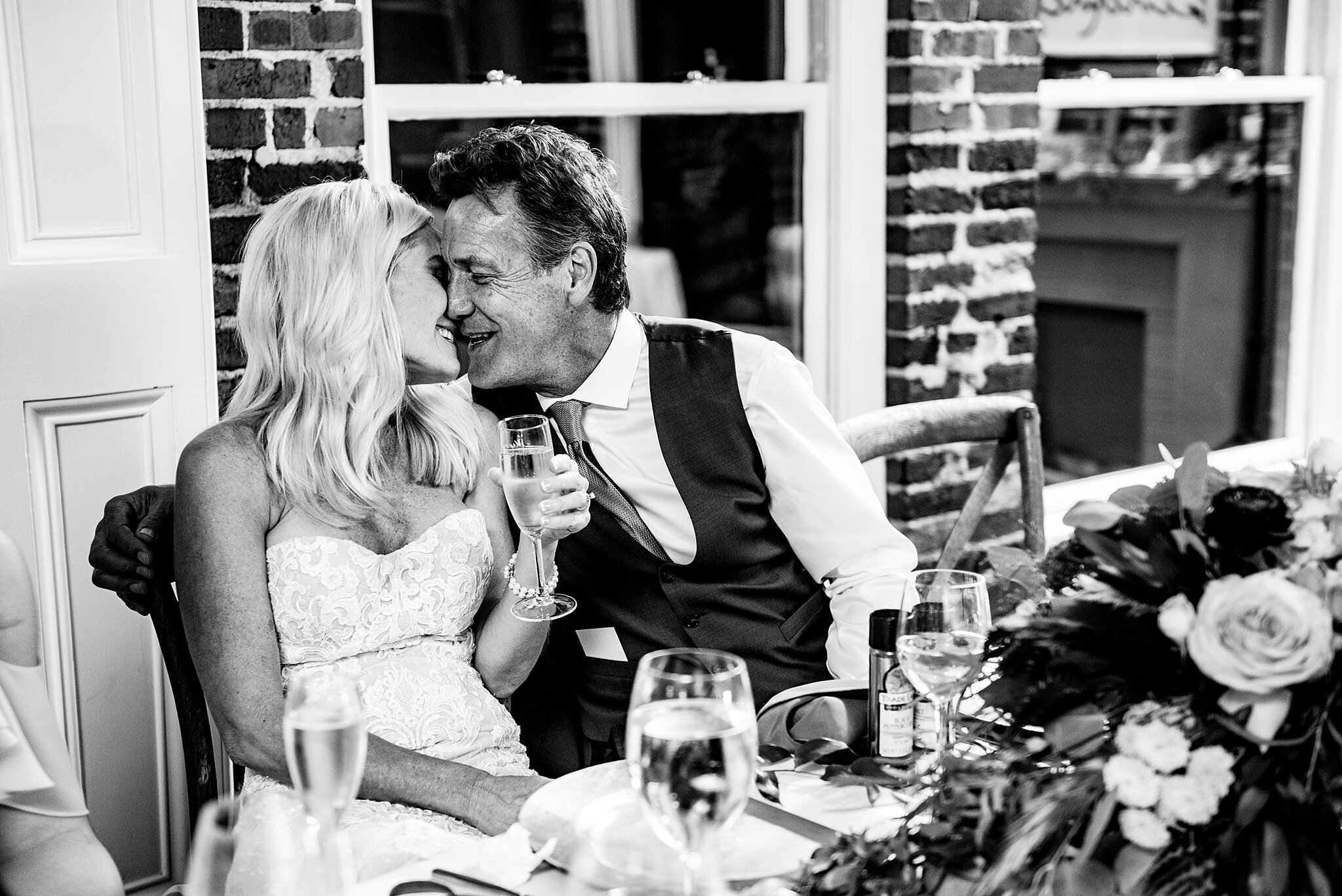 Black and White photo of bride and groom at their sweetheart table getting ready to share a kiss during toasts