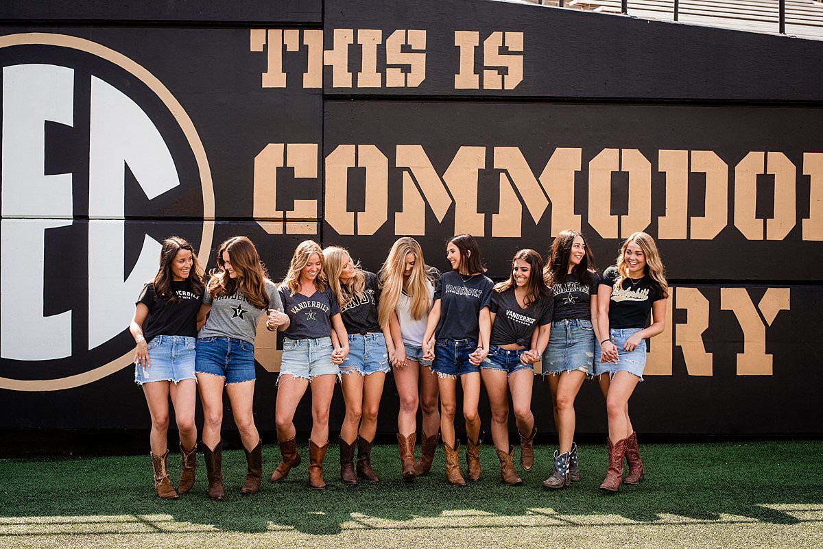 Vanderbilt College Seniors holding hands and laughing together in front of the Commodore Country sign at the football field
