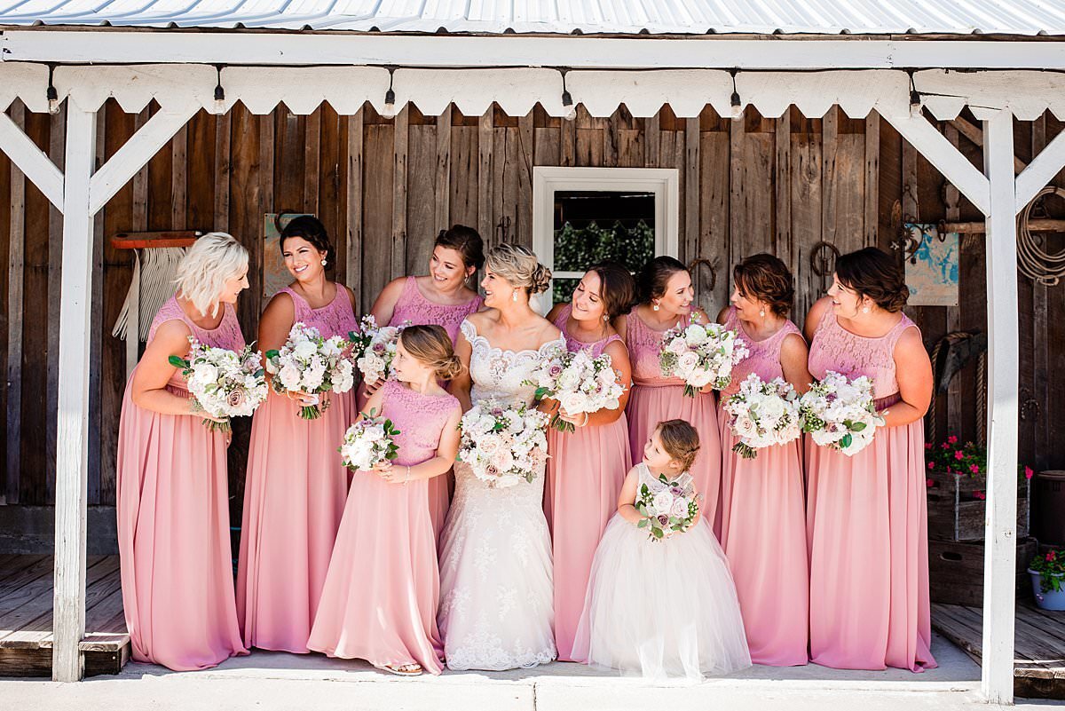 Bridesmaids wearing long pink dresses standing with bride and flowergirls on the front porch of the bridal cottage at Saddlewoods Farm