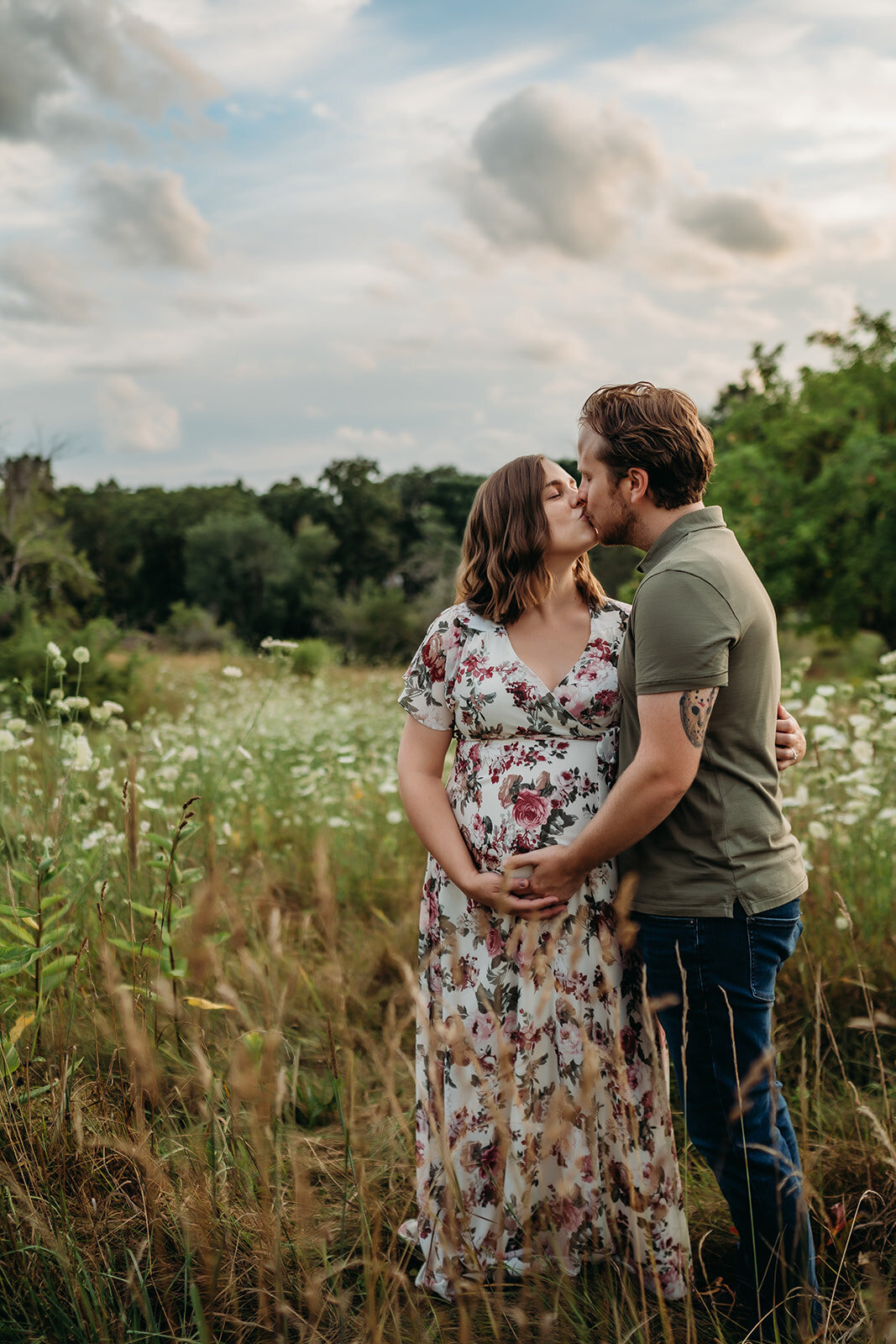 couple expecting a baby kisses in a flower field