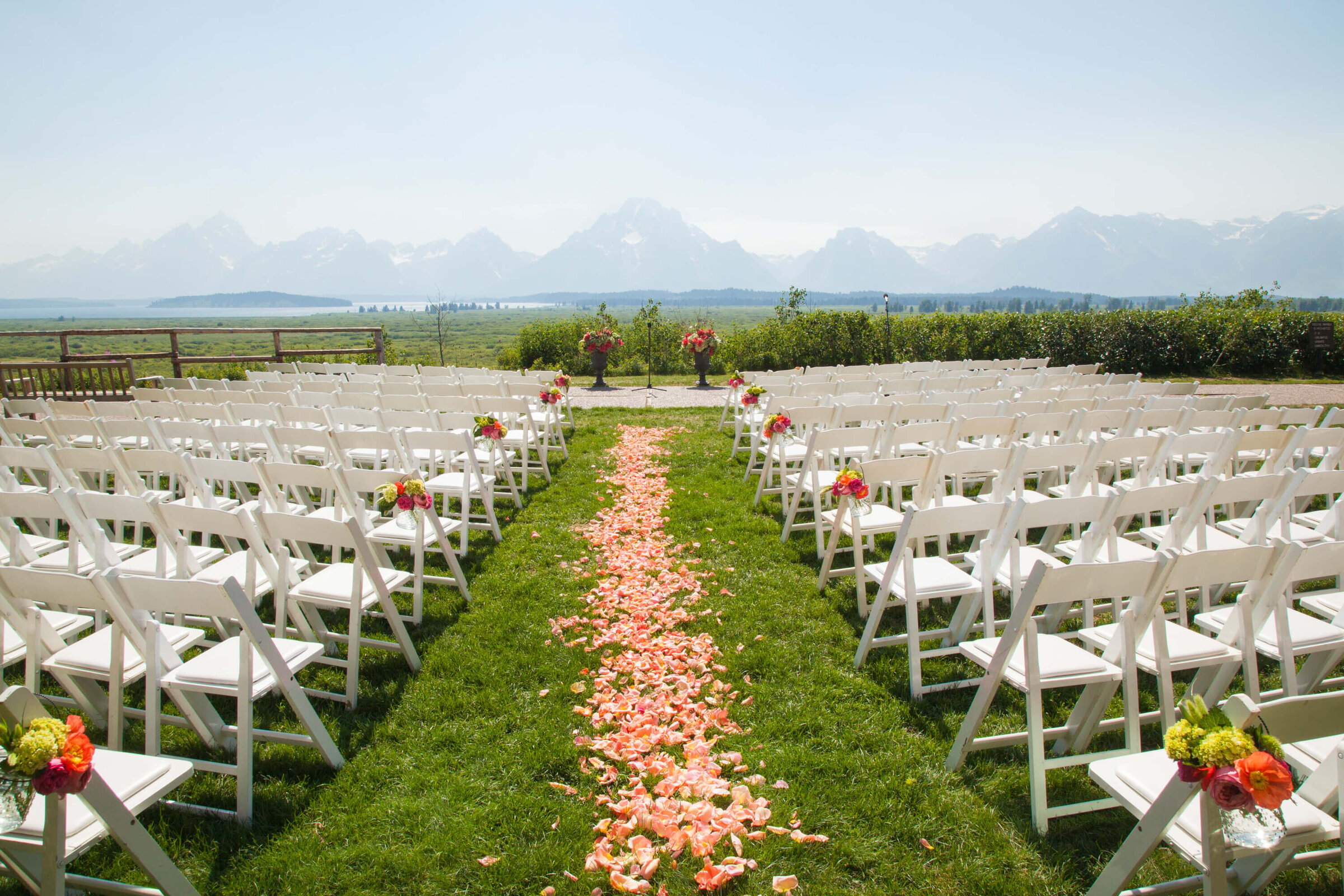 Outdoor Ceremony at Jackson Lake Lodge White chairs line a grassy aisle covered in rose petals, leading to a floral-adorned altar. The Grand Tetons provide a breathtaking backdrop for this Jackson Lake Lodge wedding ceremony.