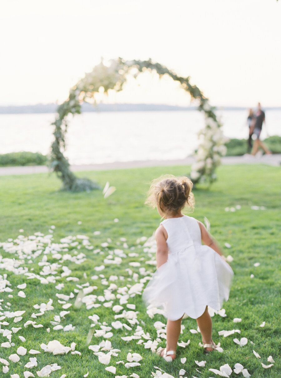flower girl on grass in white dress on lake