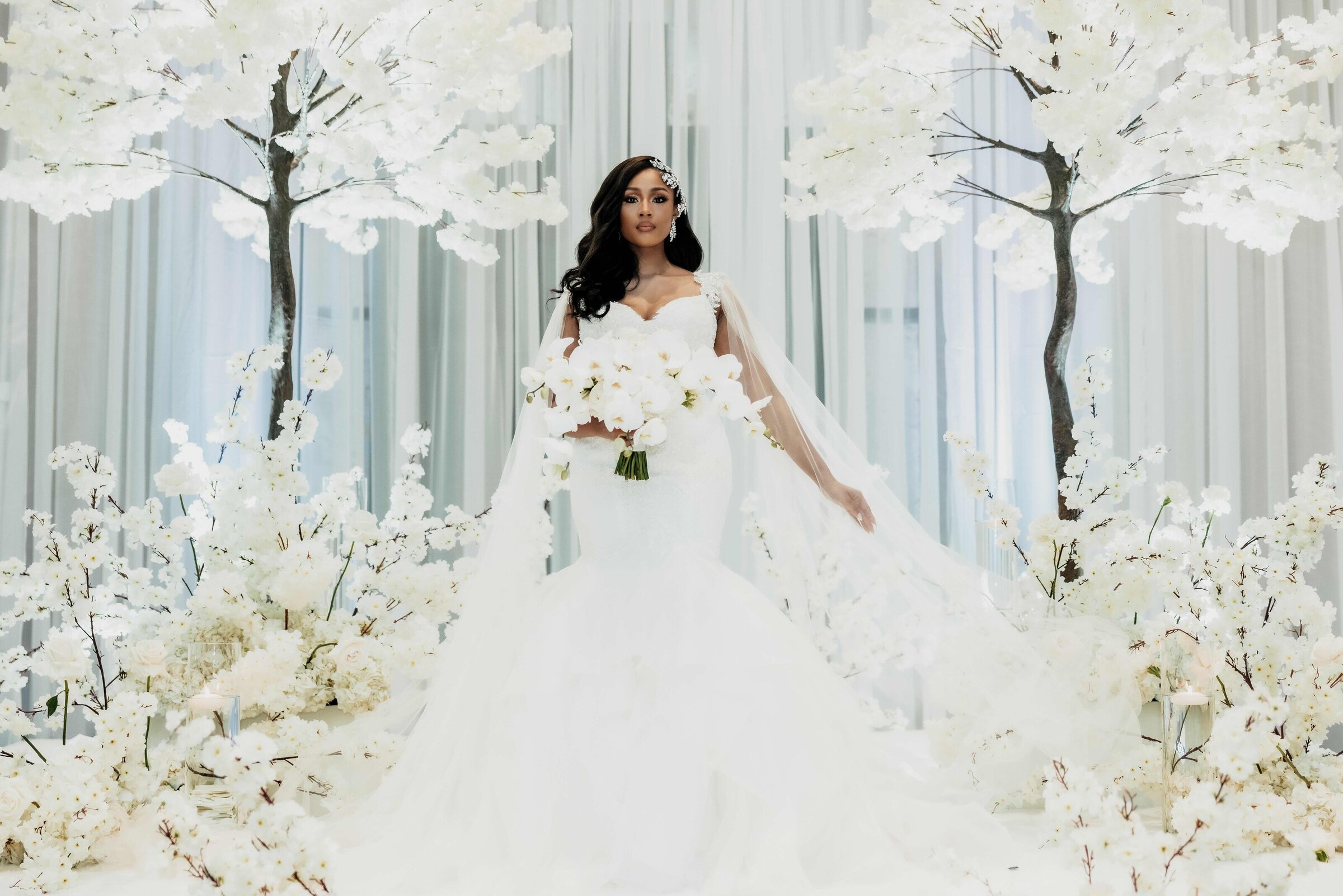 Glamorous bride holding a cascading white orchid bouquet, surrounded by luxe white floral trees at her modern wedding ceremony in downtown Nashville.