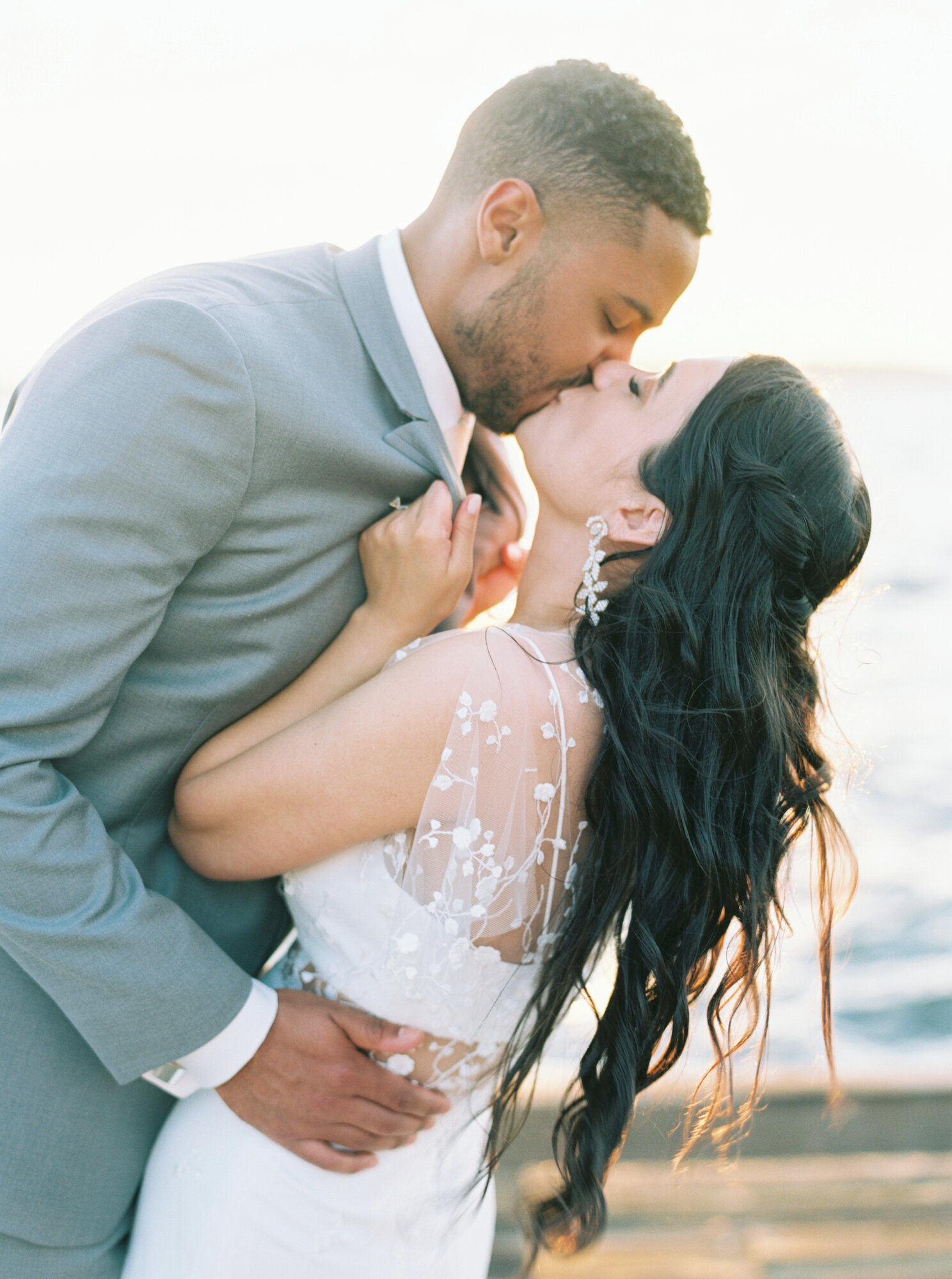 bride grabs grooms collar and brings him close for a big kiss on dock at golden hour