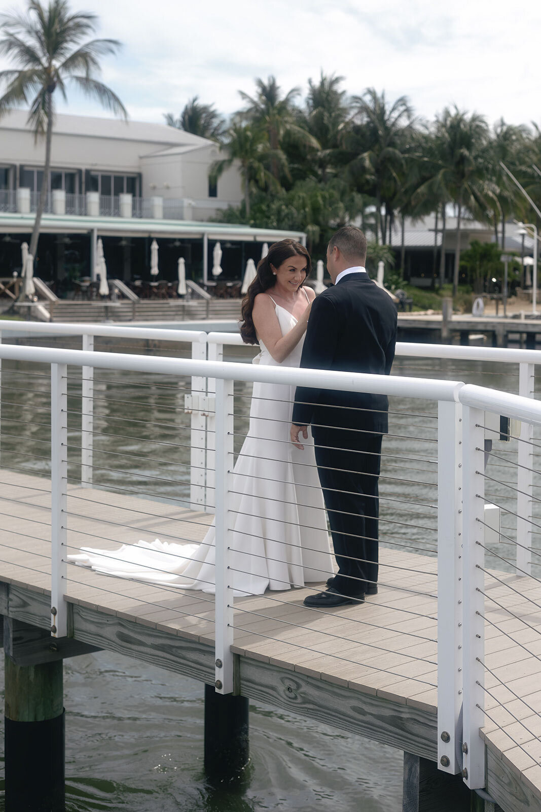 Bride and groom standing on a pier with palm trees in the background