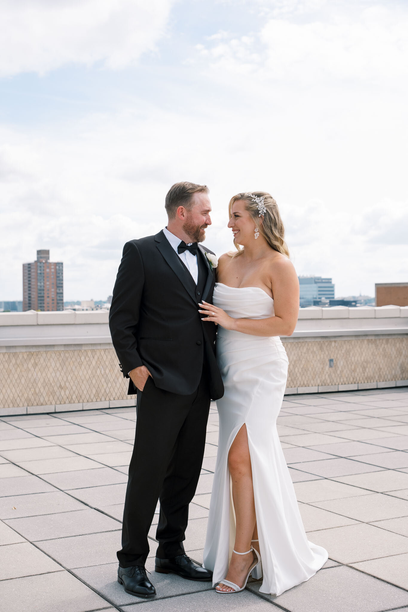 Newlyweds stand on a rooftop, gazing at each other joyfully