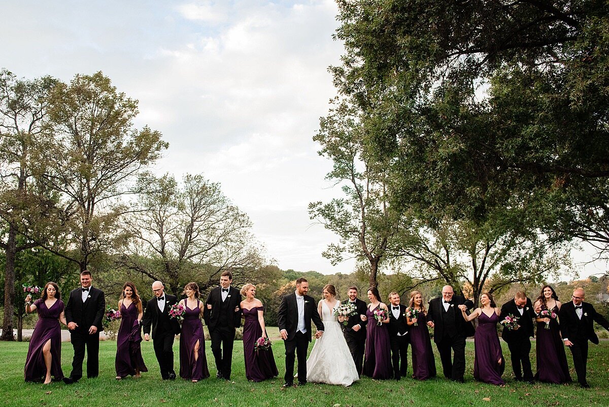 Full Wedding party walking through the open grass at Smith Park, guys are wearing classic black and white tuxedos and the bridesmaids have deep purple dresses