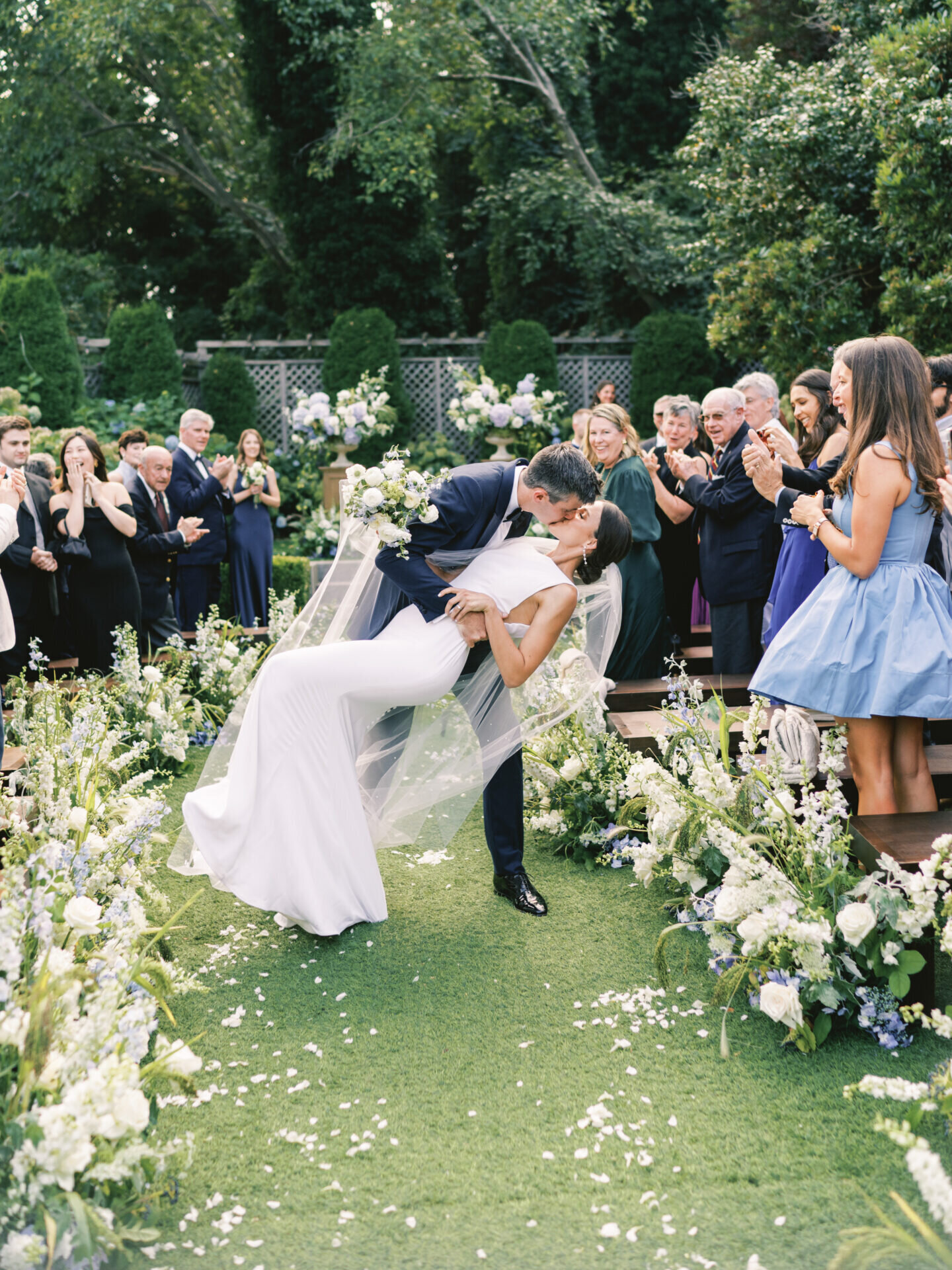 groom dips his bride and kisses her in the center of the aisle in garden ceremony