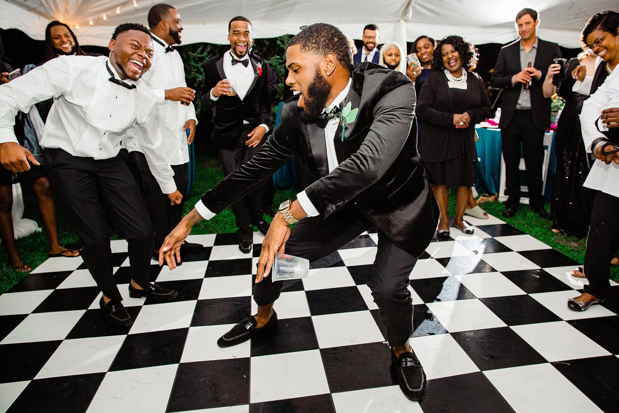 Wedding guests dancing on checkerboard dance floor at tented reception