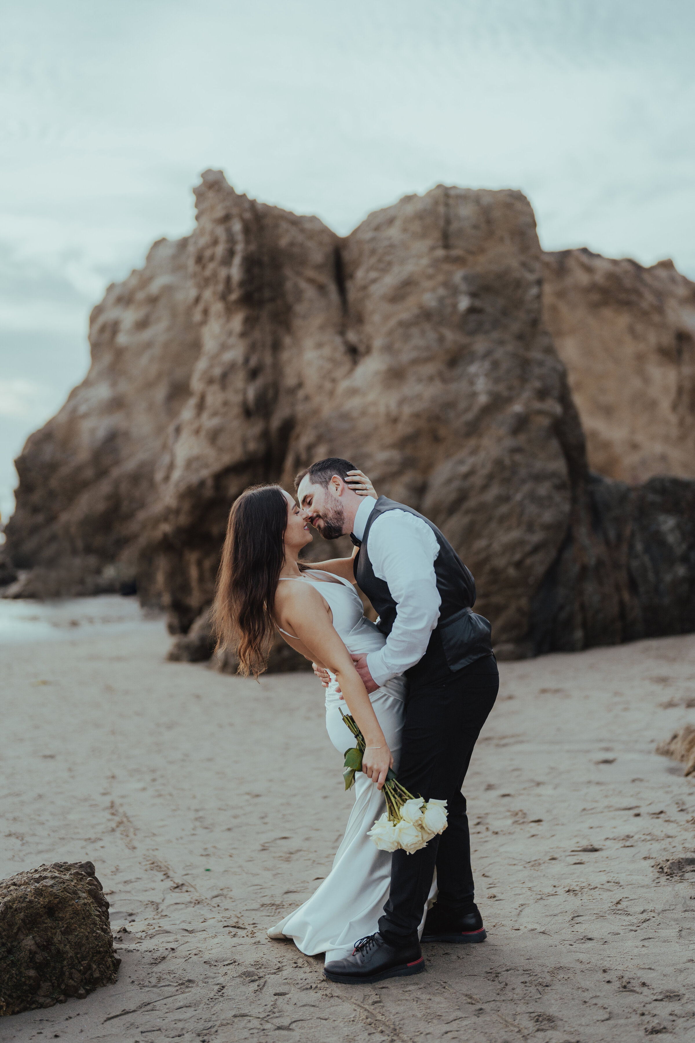 Bride and groom sharing a kiss on a Los Angeles beach, with a picturesque seascape