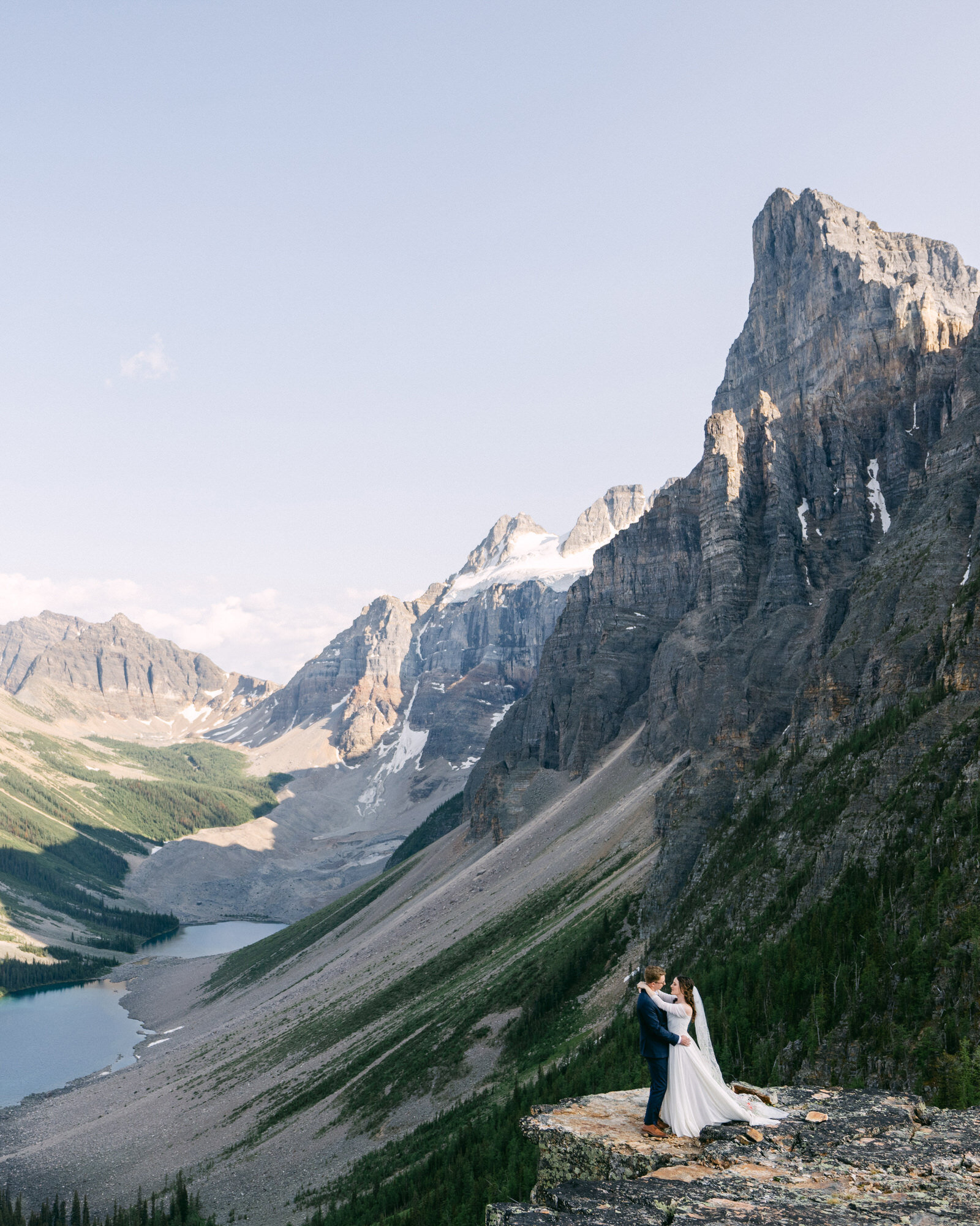 A breathtaking moment as the bride and groom hold each other after their intimate elopement in the stunning Moraine Lake region of Banff National Park. Surrounded by towering mountains and the raw beauty of the Canadian Rockies, this photograph captures the deep connection, serenity, and awe-inspiring landscape of their unforgettable day.
