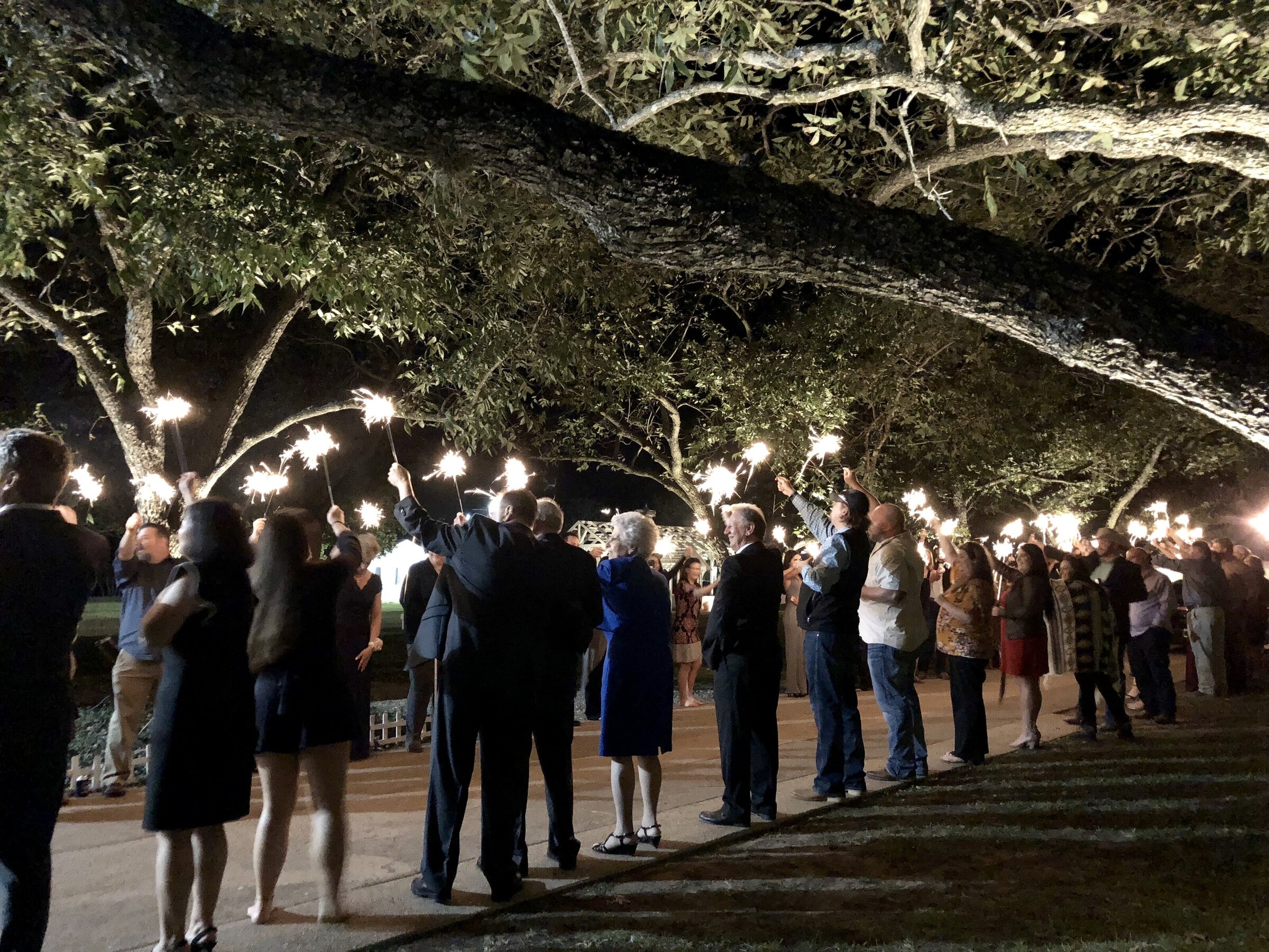 The grand exit for a wedding at the Grand Texana. Guests are holding sparklers underneath the pecan trees