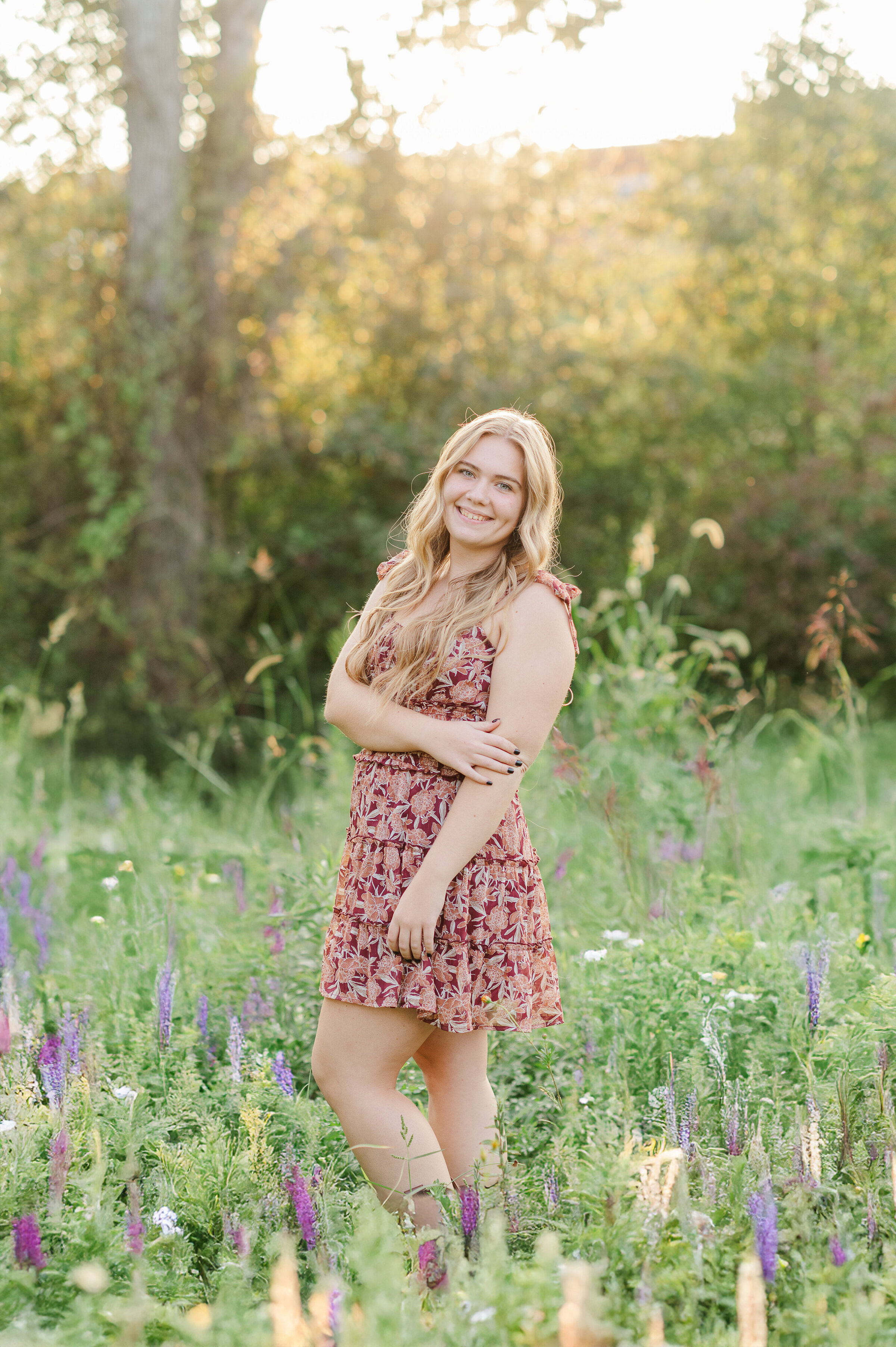 Senior girl, wearing a burgundy dress standing in wildflowers by Hershey PA photographer