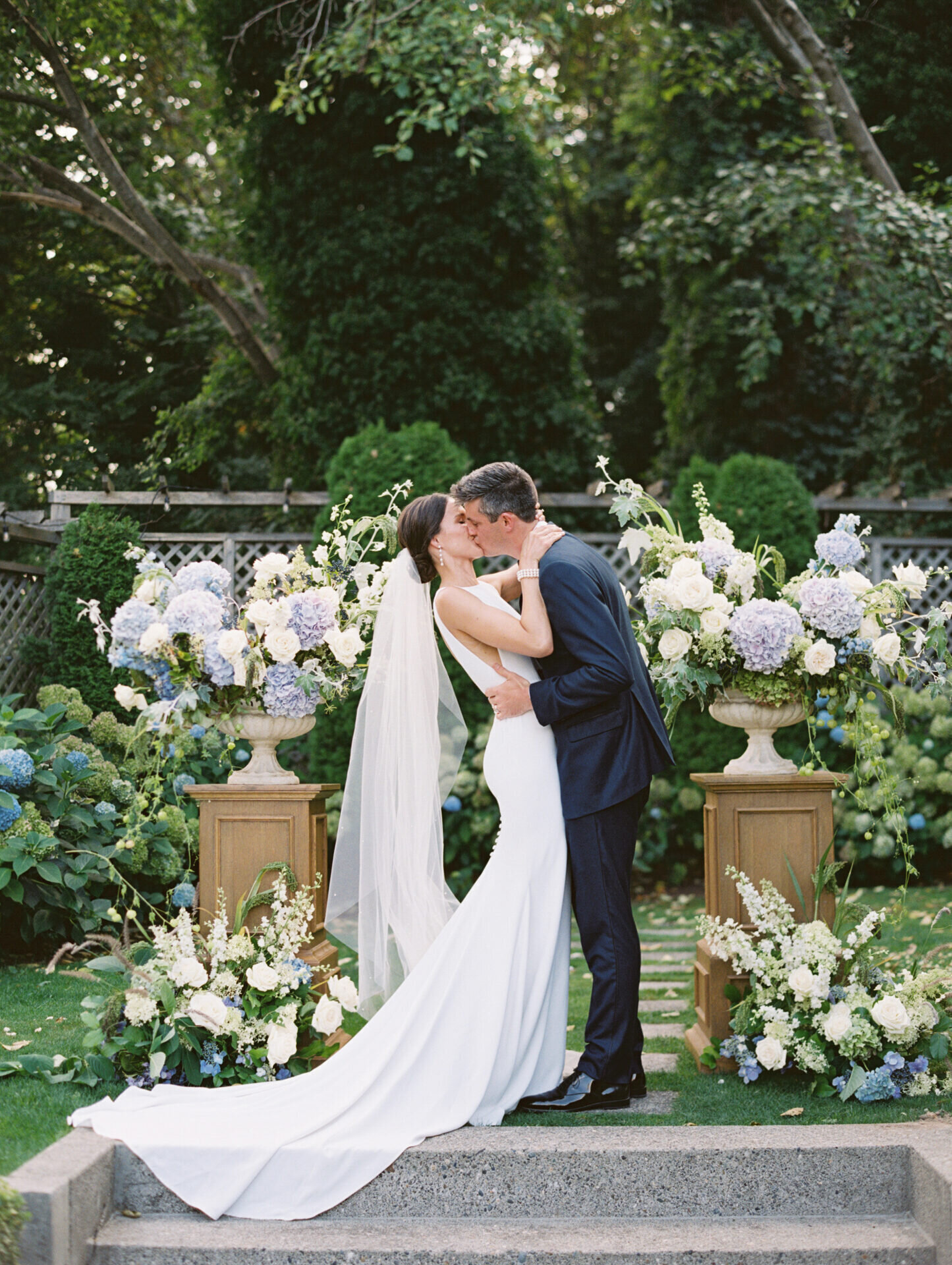 bride and groom kissing at wedding ceremony with white purple and blue floral arrangements surrounding them
