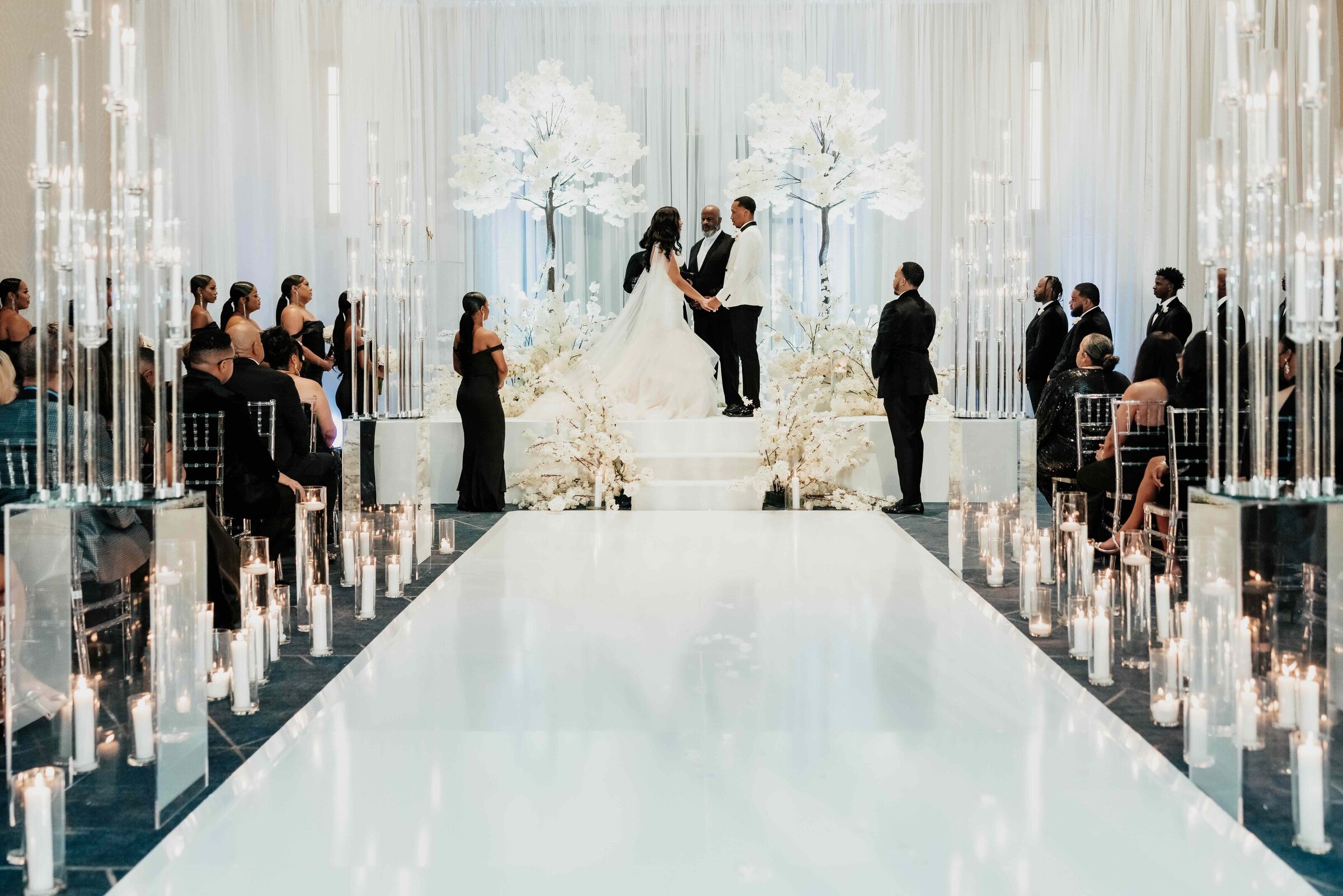 Bride and groom exchange vows at JW Marriott Nashville surrounded by glowing candles, white cherry blossom trees, and a glamorous modern ceremony design.