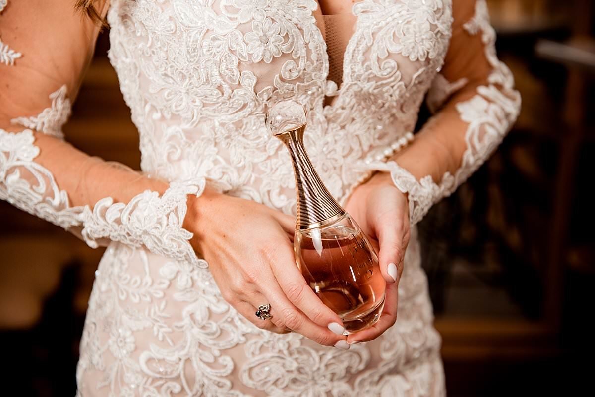 Close up image of Bride wearing lace wedding dress holding a perfume bottle