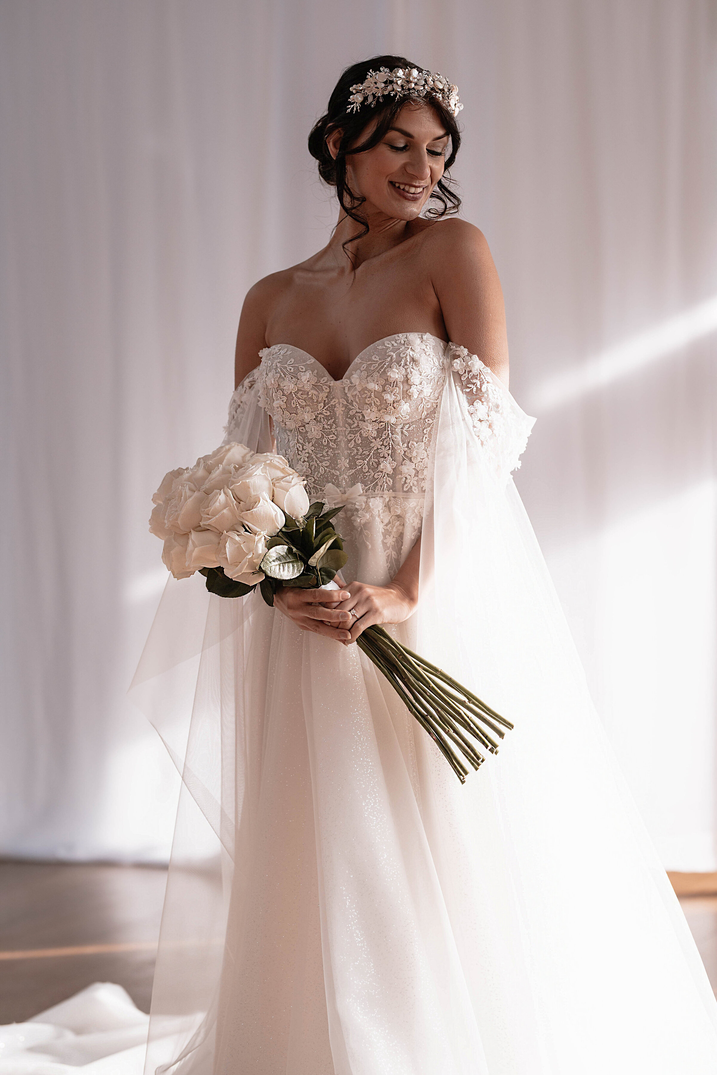 Bride in lace and sparkly wedding dress smiling and holding bouquet of white roses