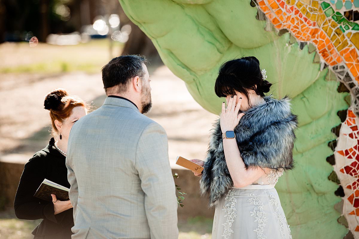 Bride tearing up while saying her vows, the couple is standing under the dragon instillation in the park in Nashville