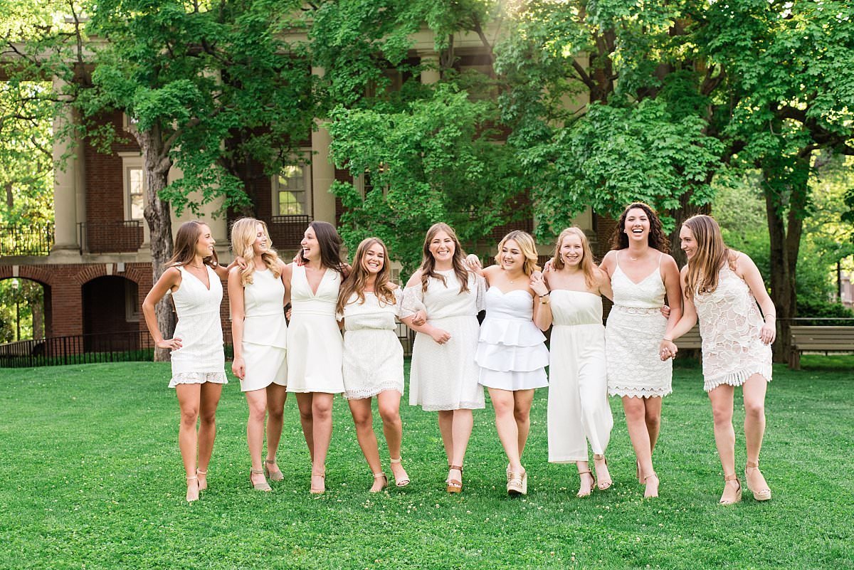 Kappa Kappa Gamma sisters linked arms walking across grassy campus wearing different white dresses
