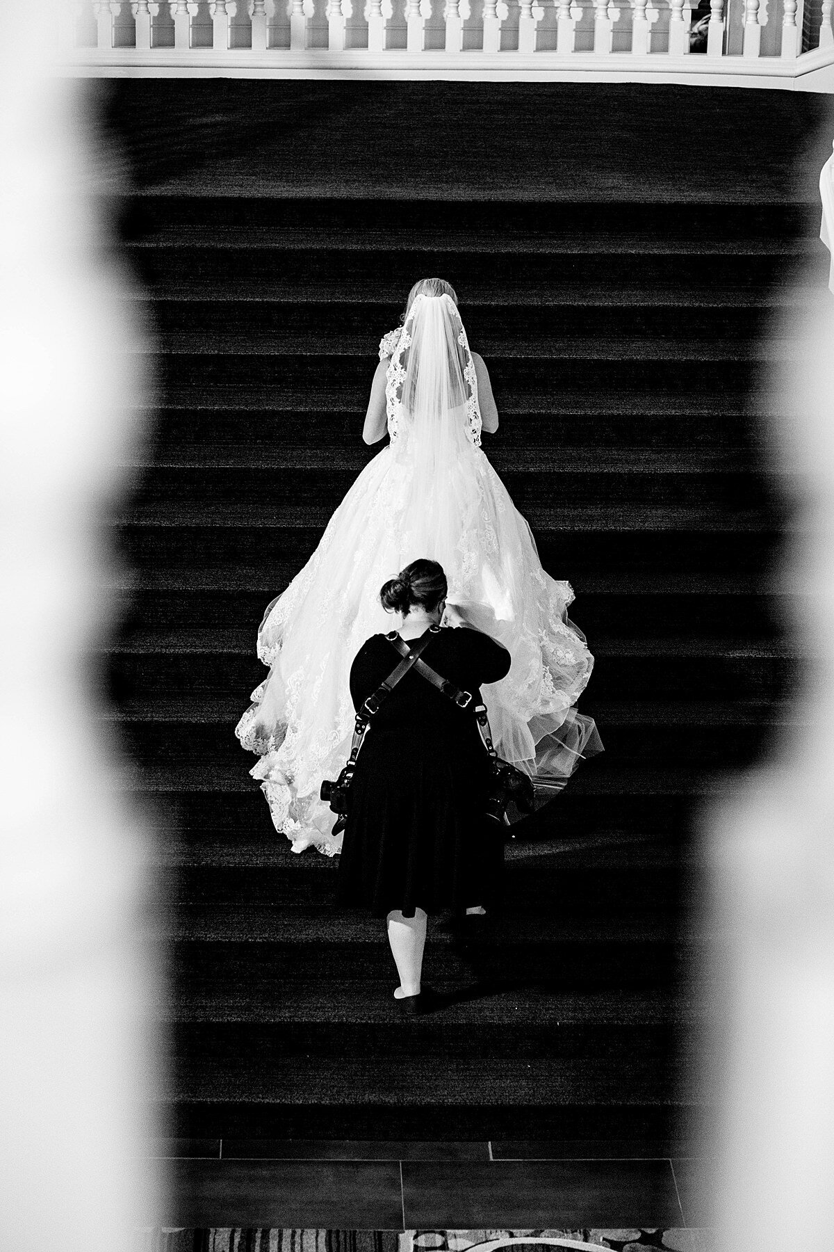Black and White photo of Mahlia helping bride with her train as she walks up the stairs