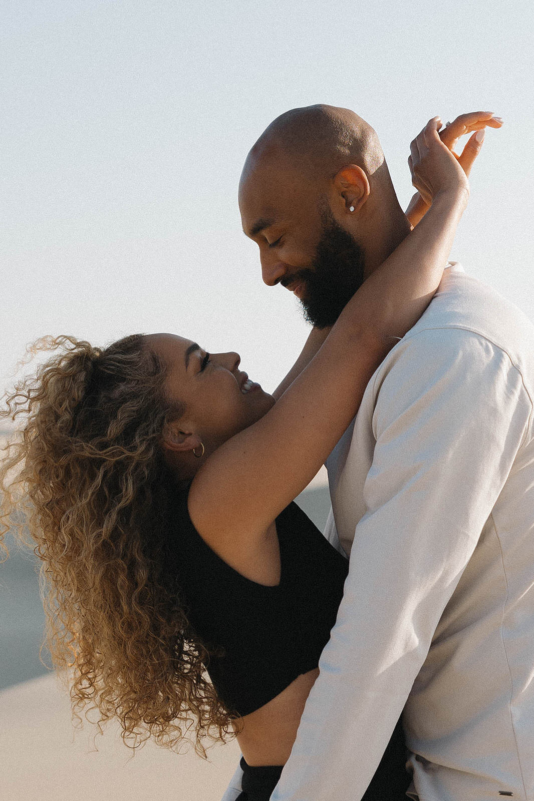 Engaged couple laughing and embracing in the sand dunes