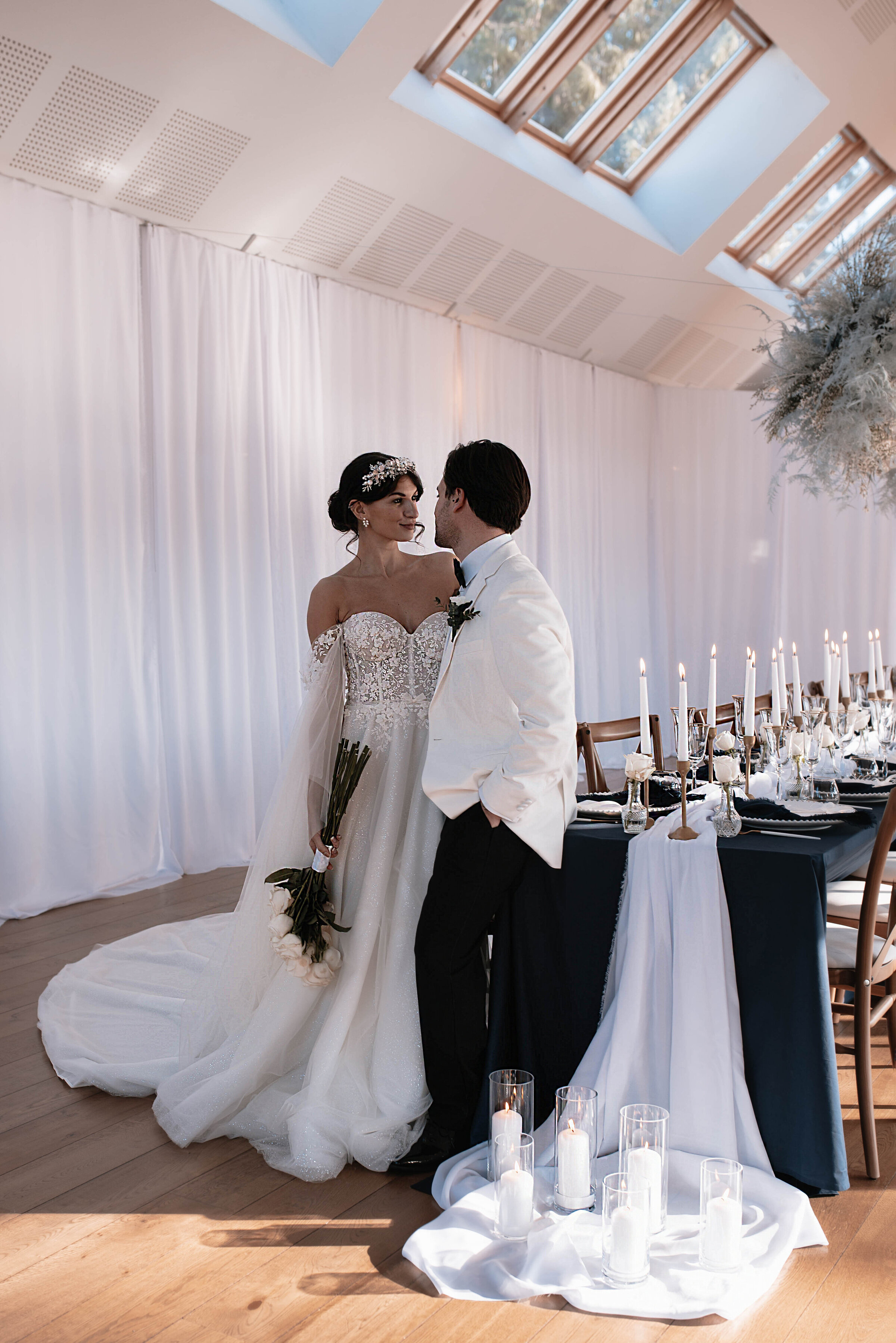 Bride and Groom in wedding attire standing together in front of wedding breakfast table at Larmer Tree Gardens in Wiltshire