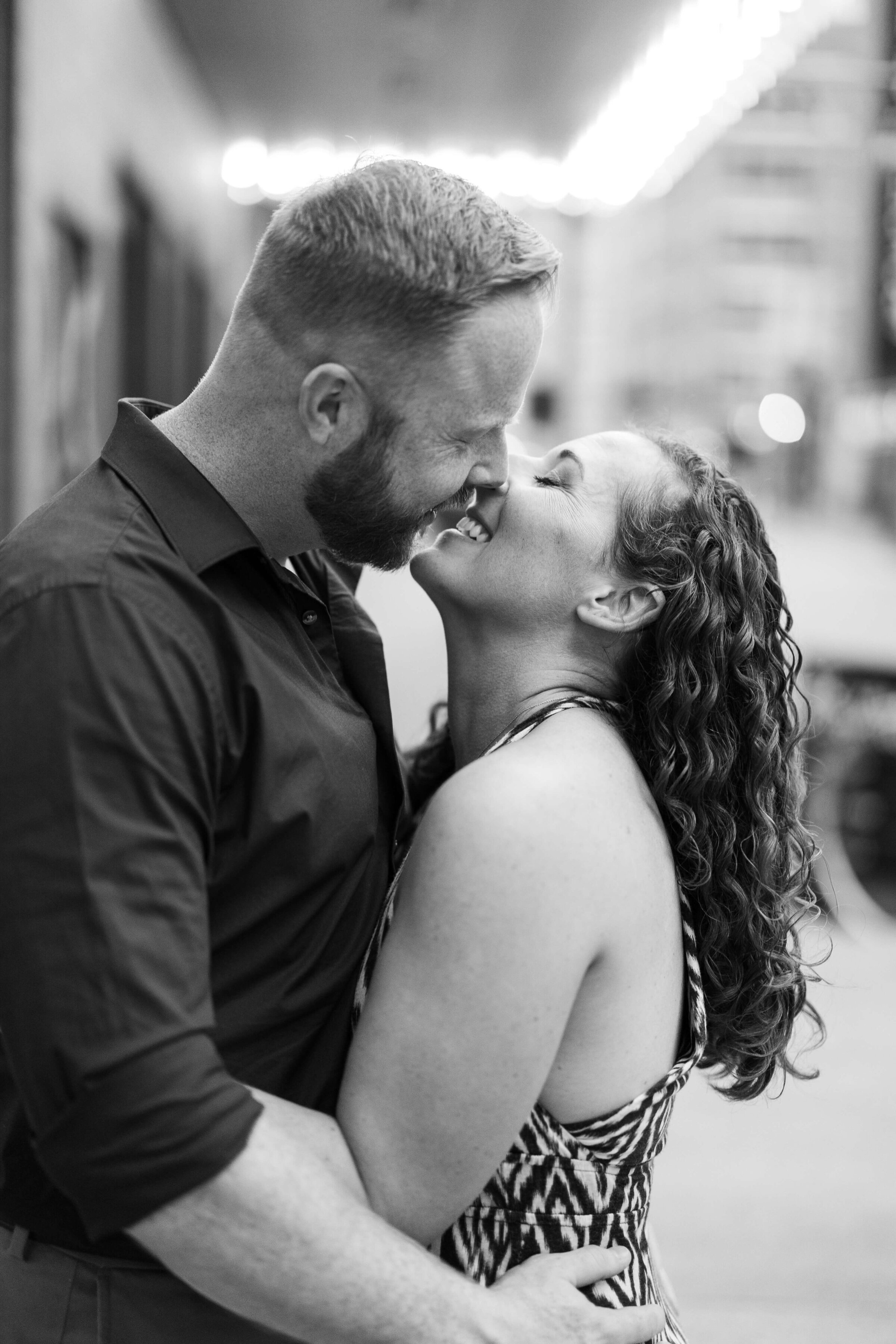 A man and woman almost kiss and laugh together. It's a black and white photo. They are in downtown cincinnati.