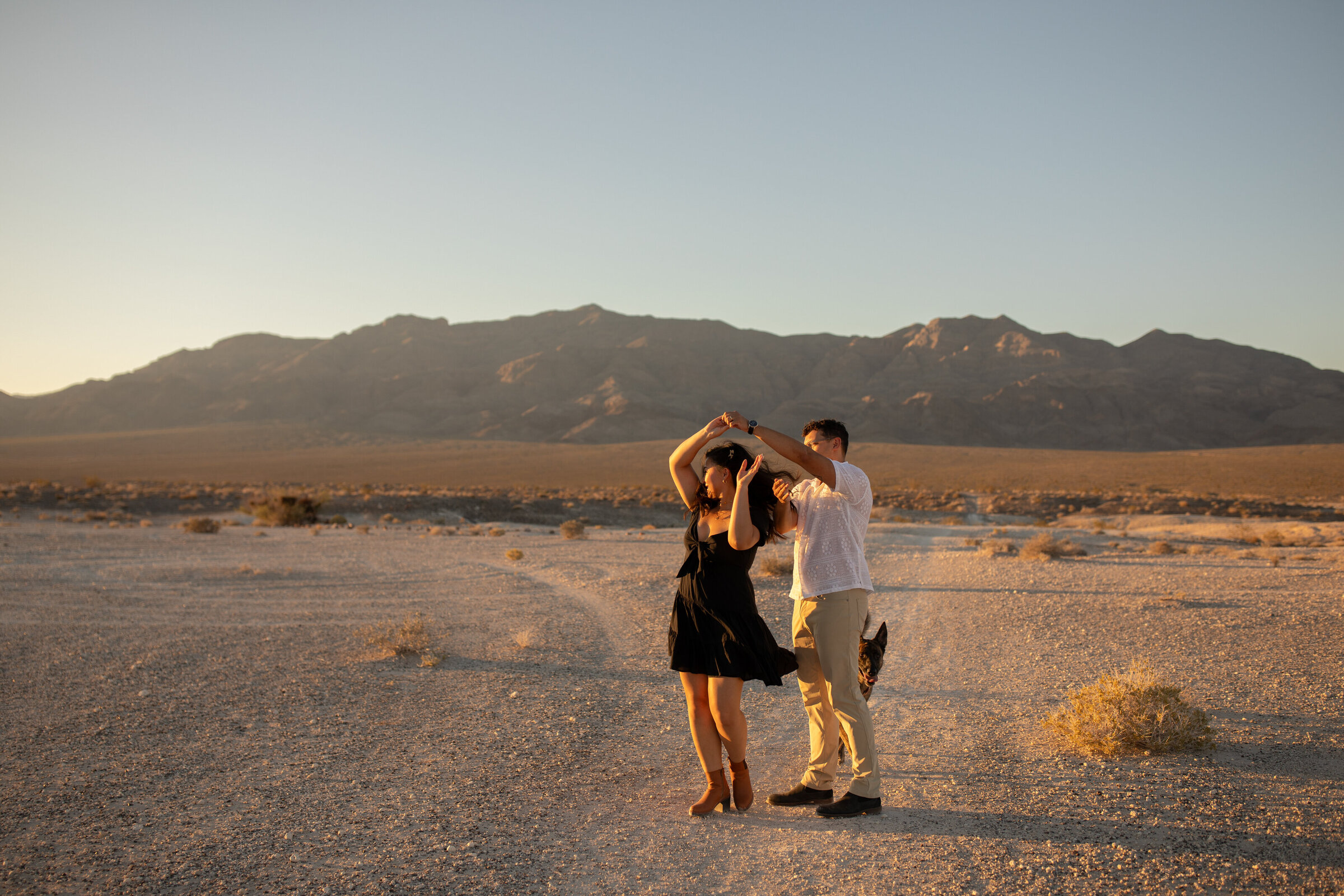 couple dancing in front of las vegas mountains during sunset with their dog taken by las vegas based portrait photographer alexis dean