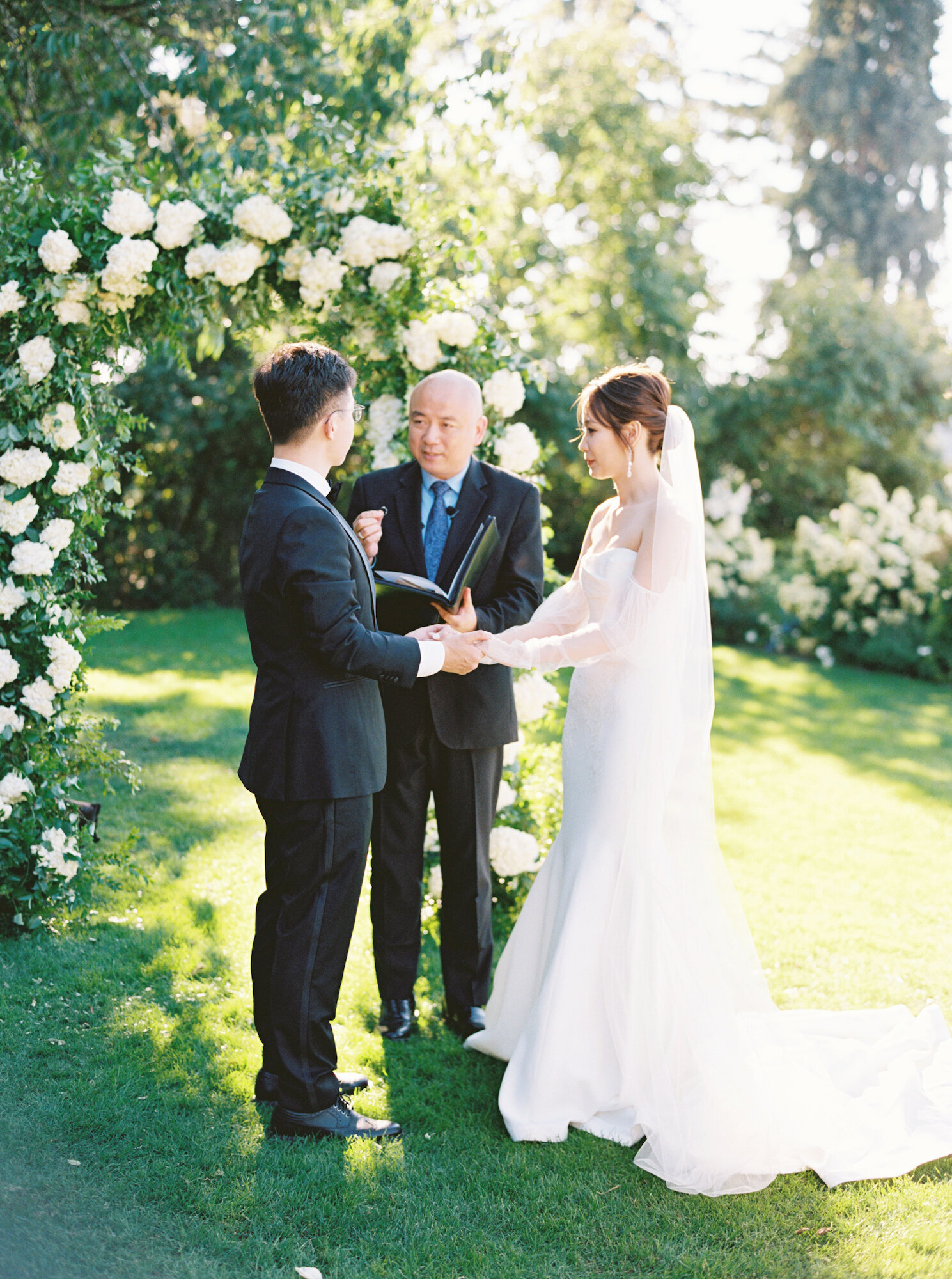 bride and groom in green garden ceremony with white hydrangea arch