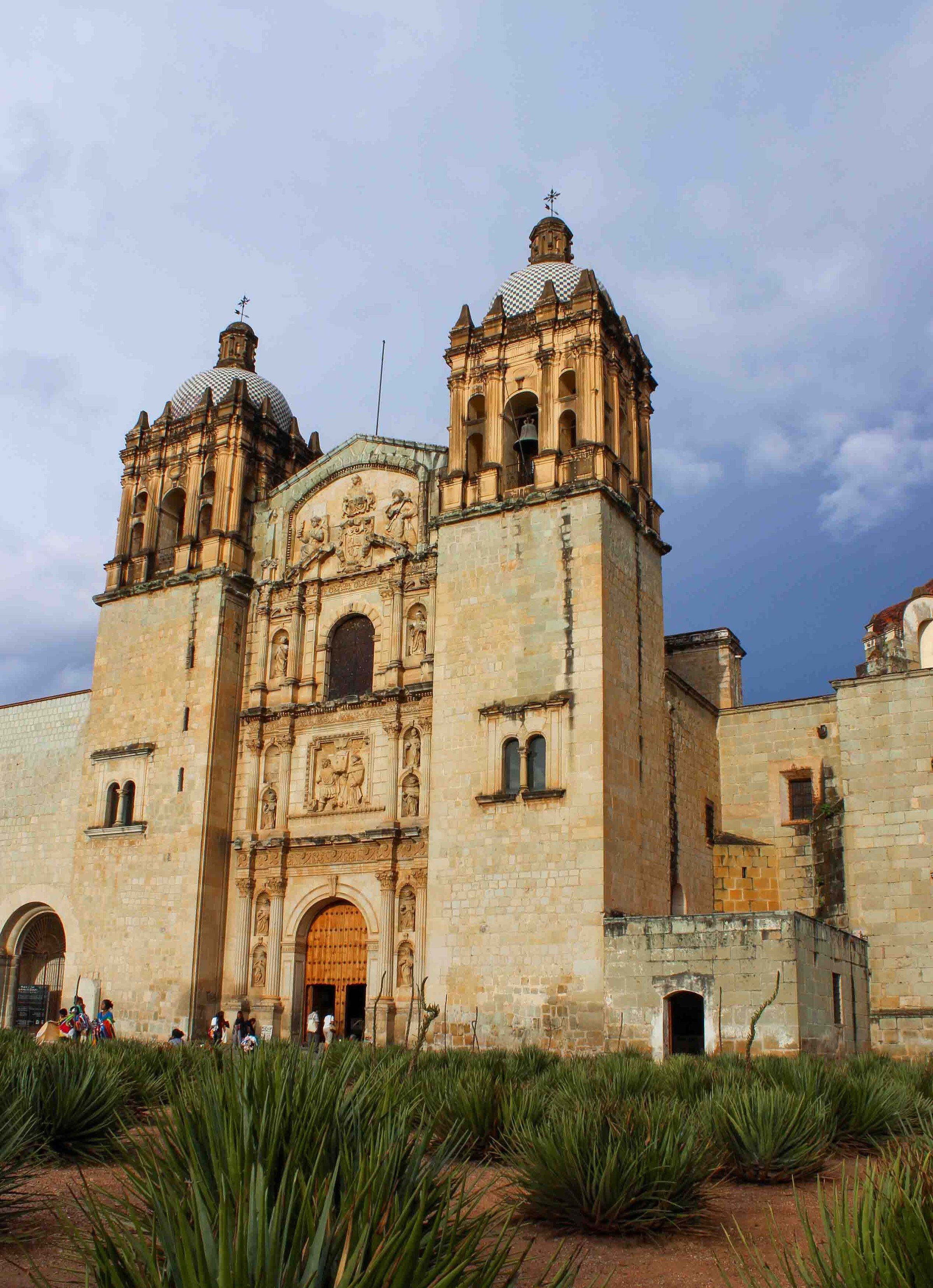 The green-stone facade of the Templo de Santo Domingo church, with agave plants in the foreground, in Oaxaca, Mexico ©Stephanie Dosch | theViatrix Luxury Travel
