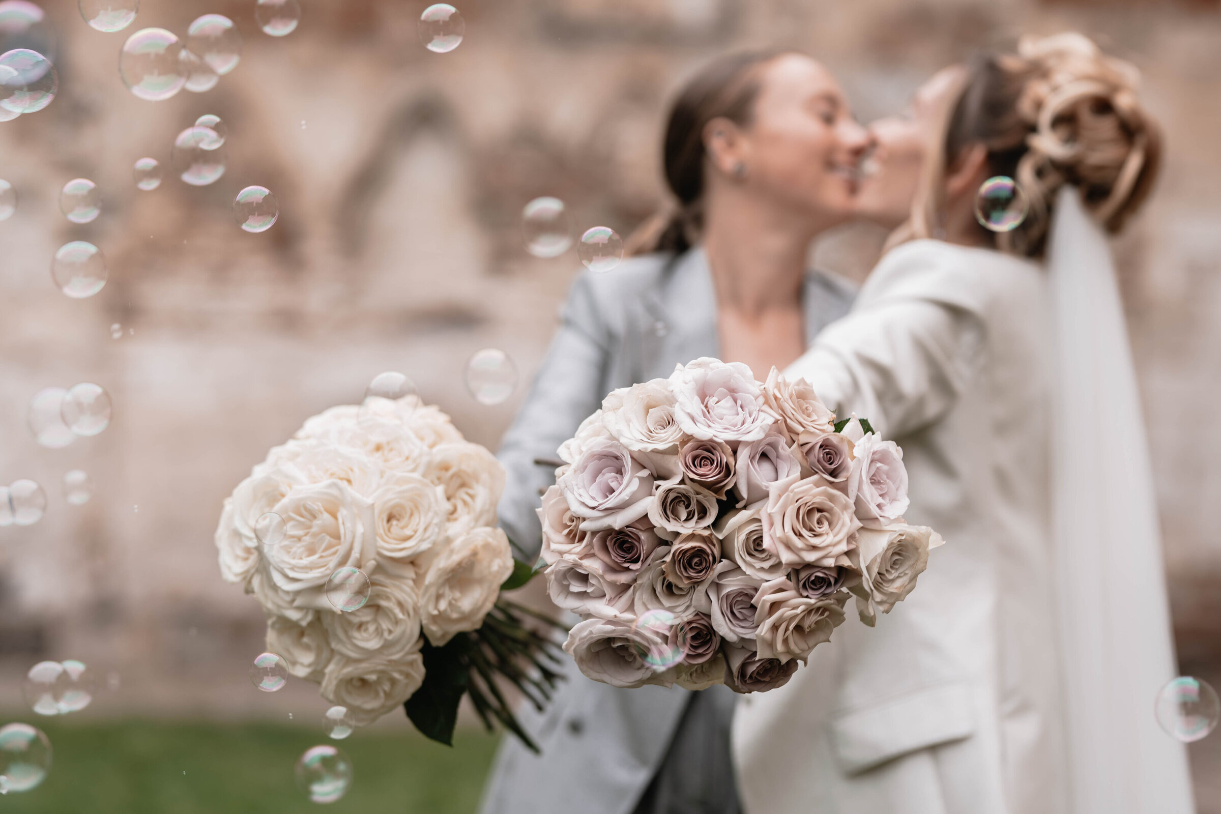 Two brides blurred in the background holding out bouquets of roses which are in focus in the forerground