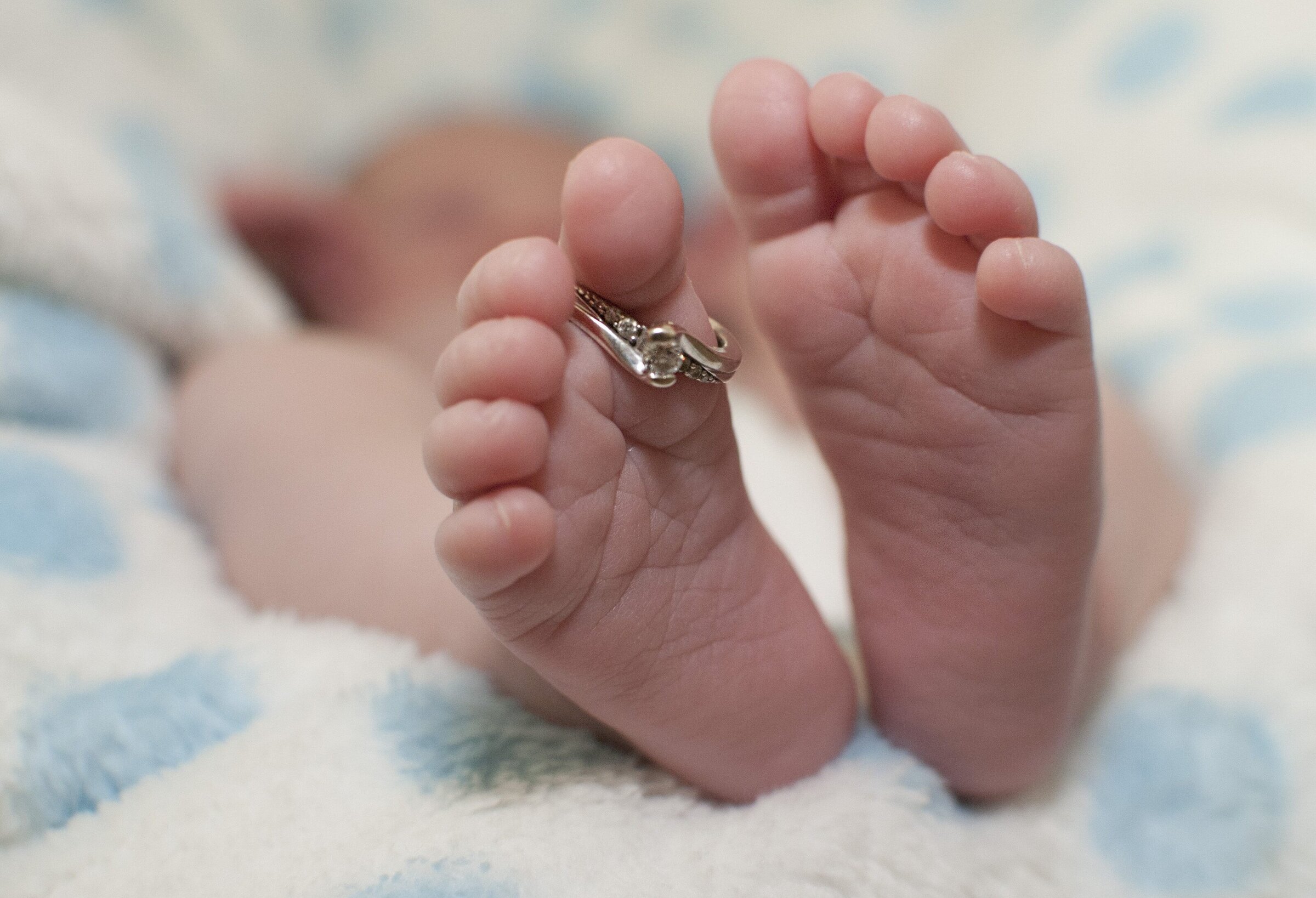 Close up off a newborn baby's feet with mum's engagement ring hanging from their toe