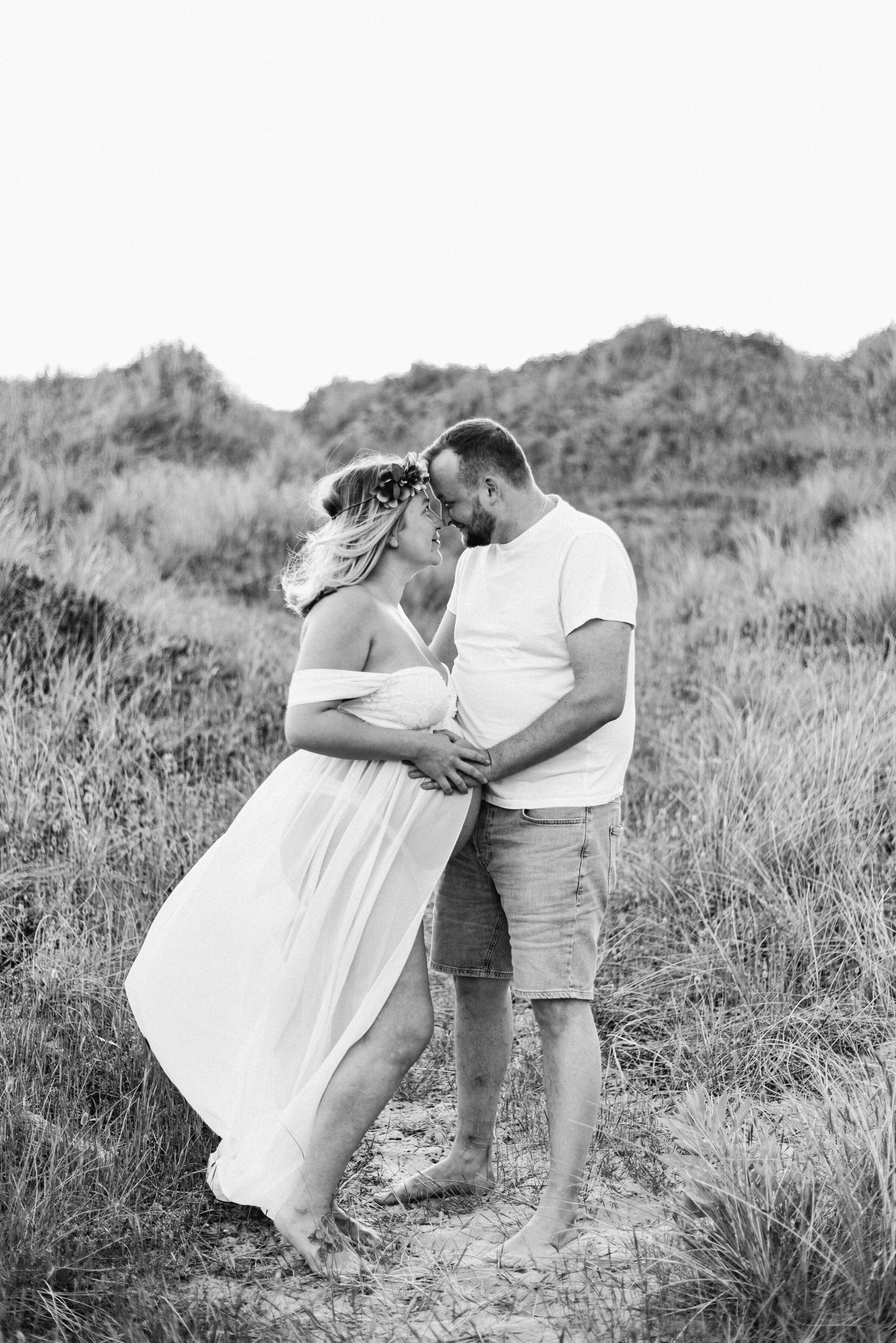 A women and man holding hands with their faces touching at the beach at billingshurst maternity photoshoot