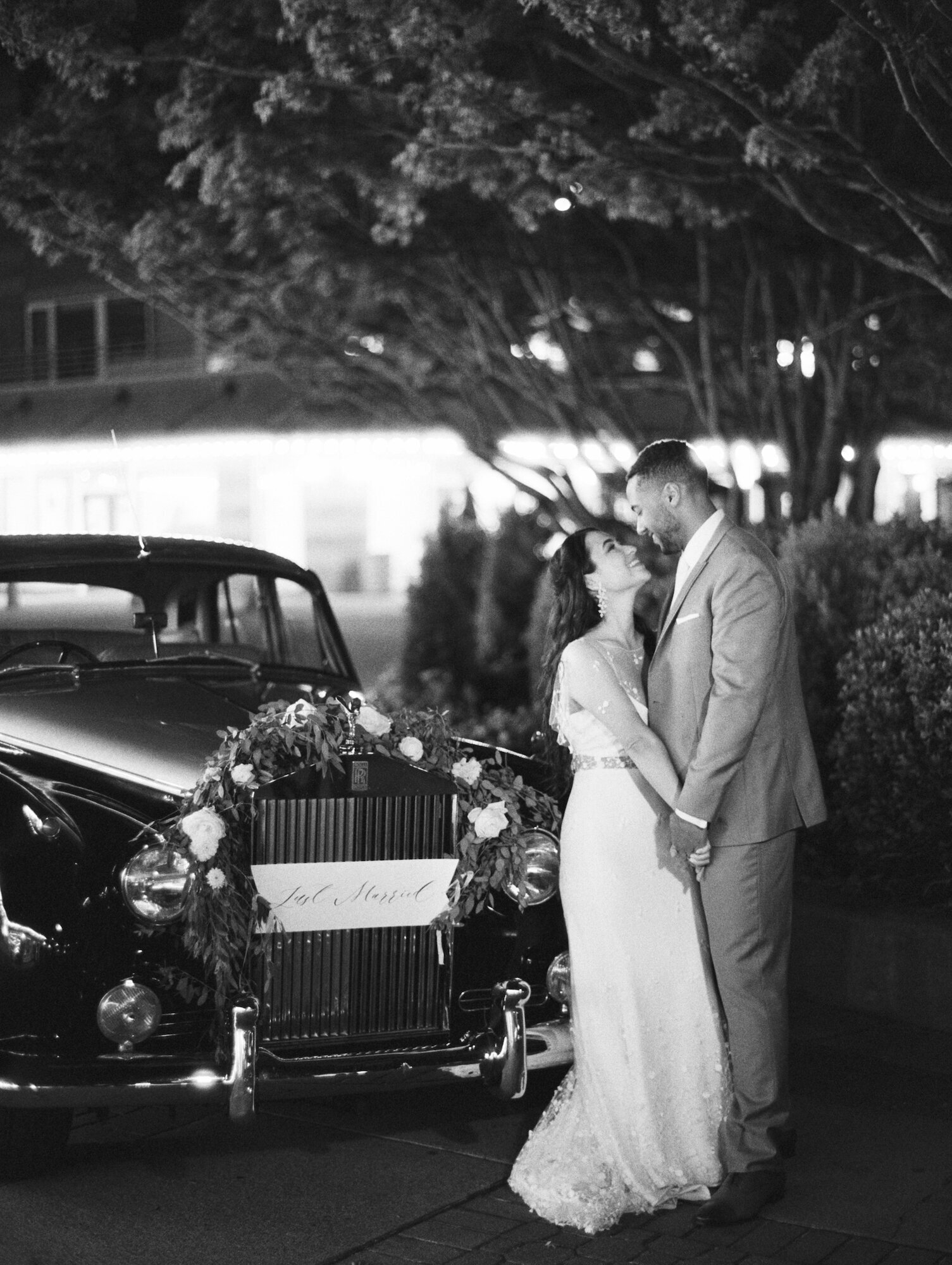 bride and groom in black and white next to rolls royce getaway car