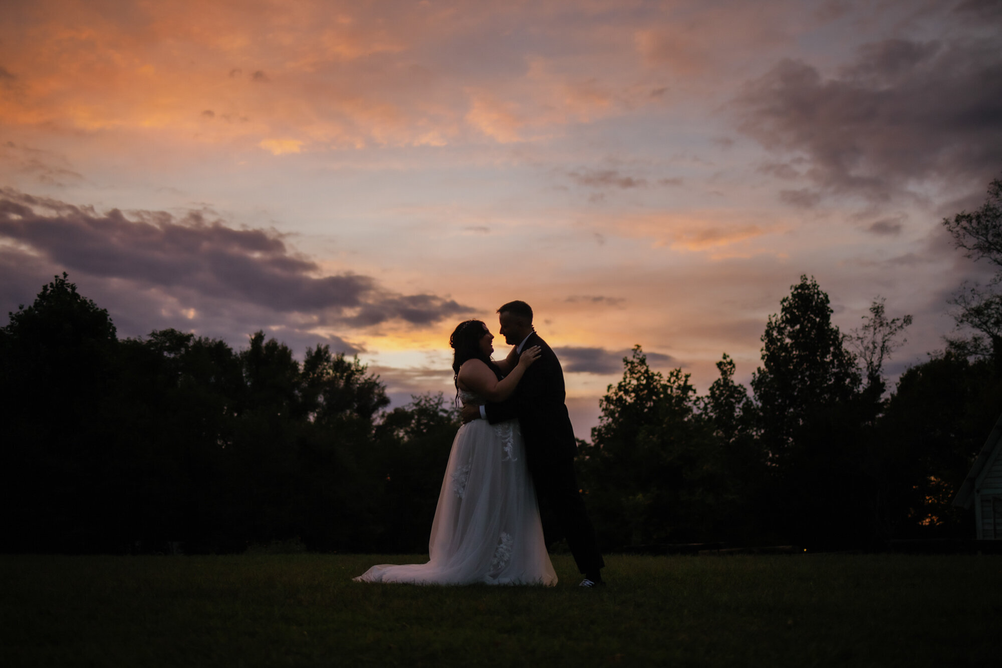 Gatlinburg elopement with bride adn groom embracing in a field after sunset with their silhouettes with the line of trees behind them