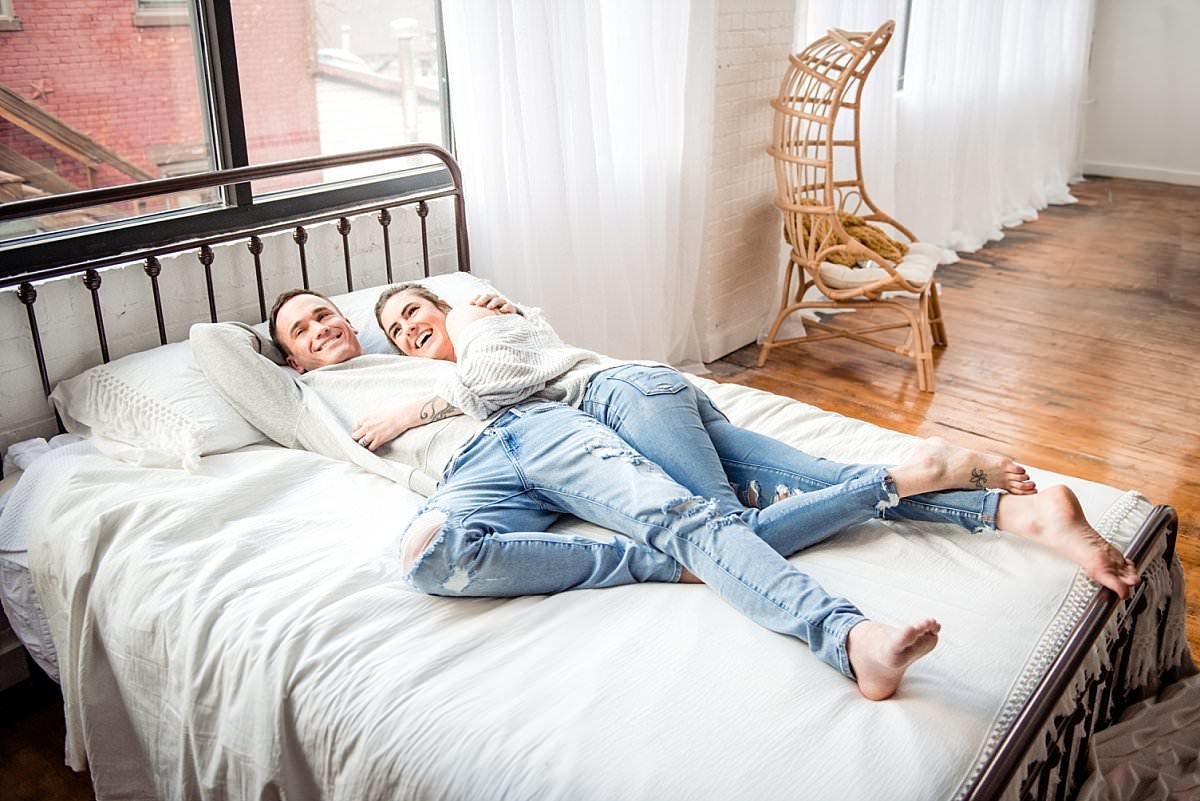 Couple lounging together on their bed wearing casual light colored jeans and white tops