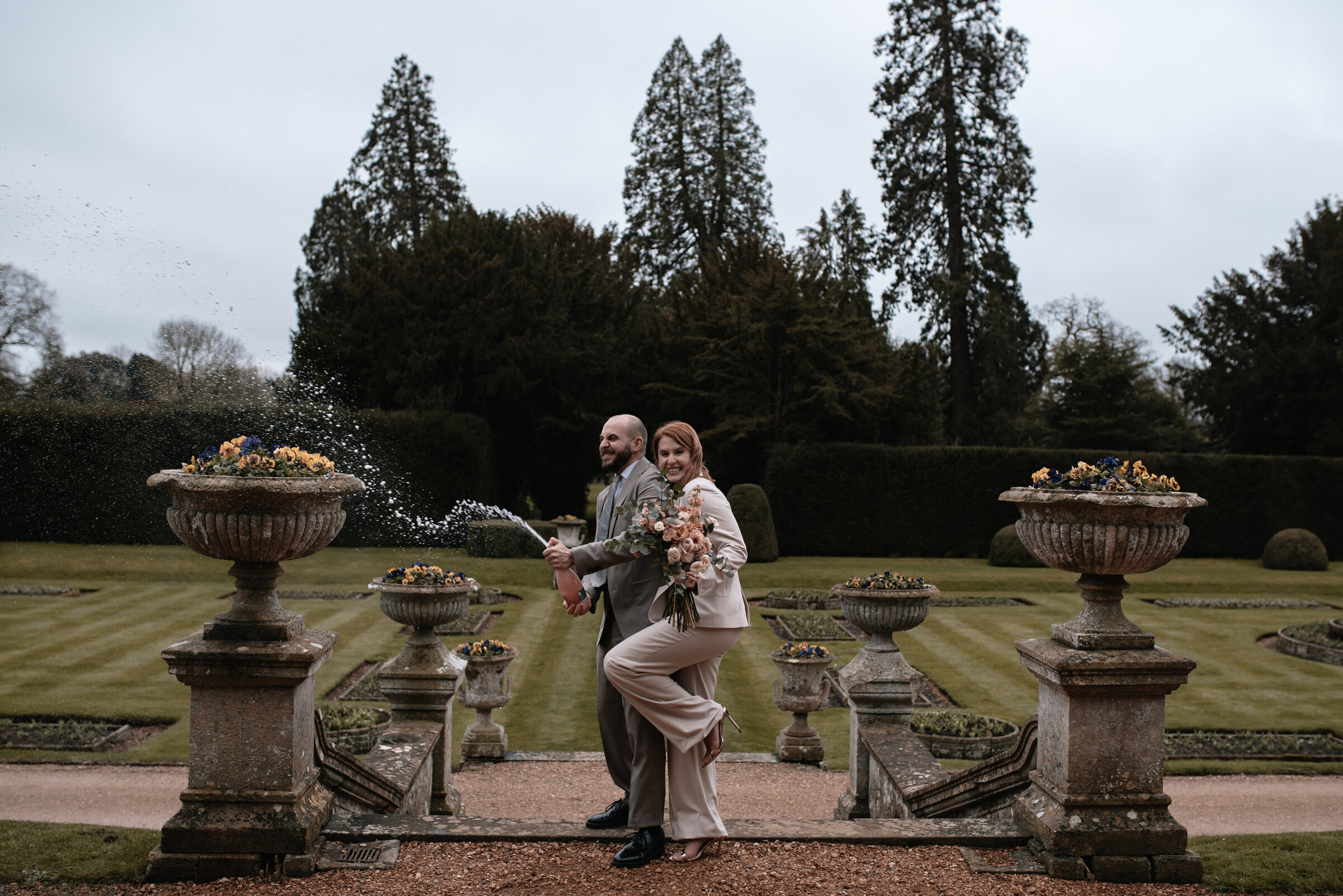 Bride and Groom spraying champagne  at the top of the steps in the gardens at Grittleton House wedding venue in Wiltshire