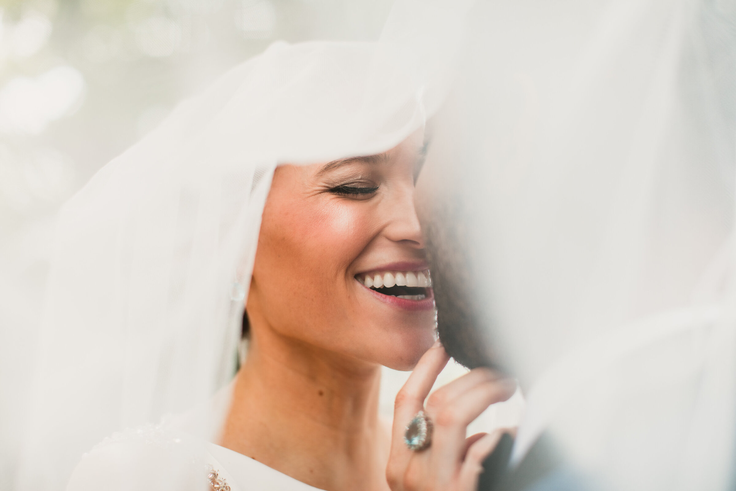 bride hdiing under her wedding veil kissing groom